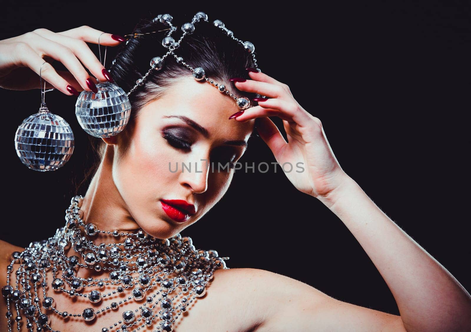 beautiful woman with dark makeup and red lipstick posing on black background. Wearing silver disco ball jewllery.