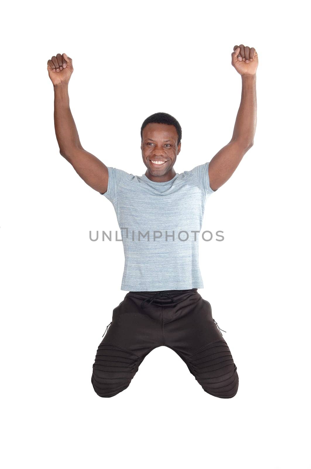 A young handsome African American man kneeling on the floor with.his fists and smiling of victory and success, isolated over white.