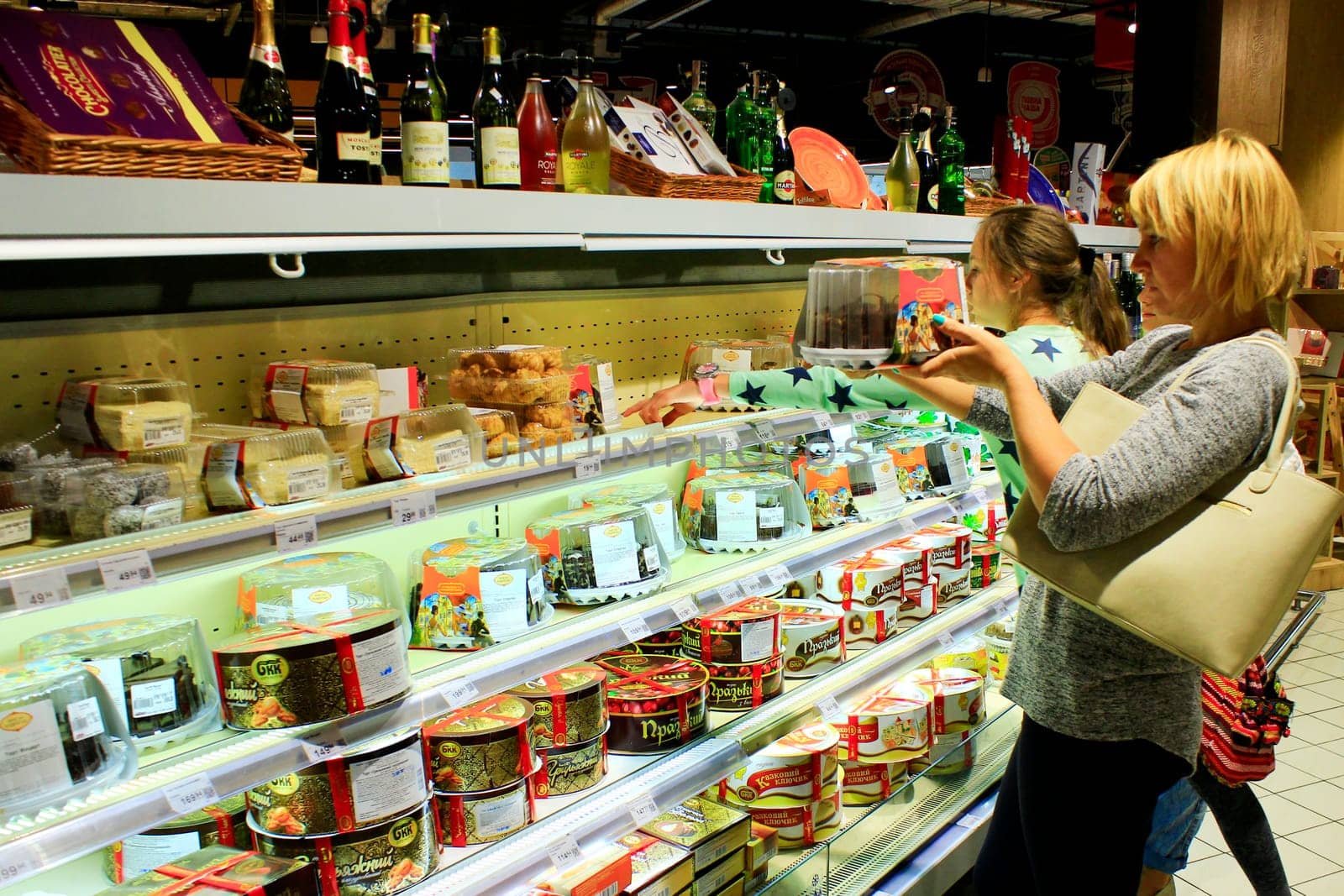 Mother and her daughter choicing cake on shelves of supermarket. Shopping of dessert. Buying food. Family in shop