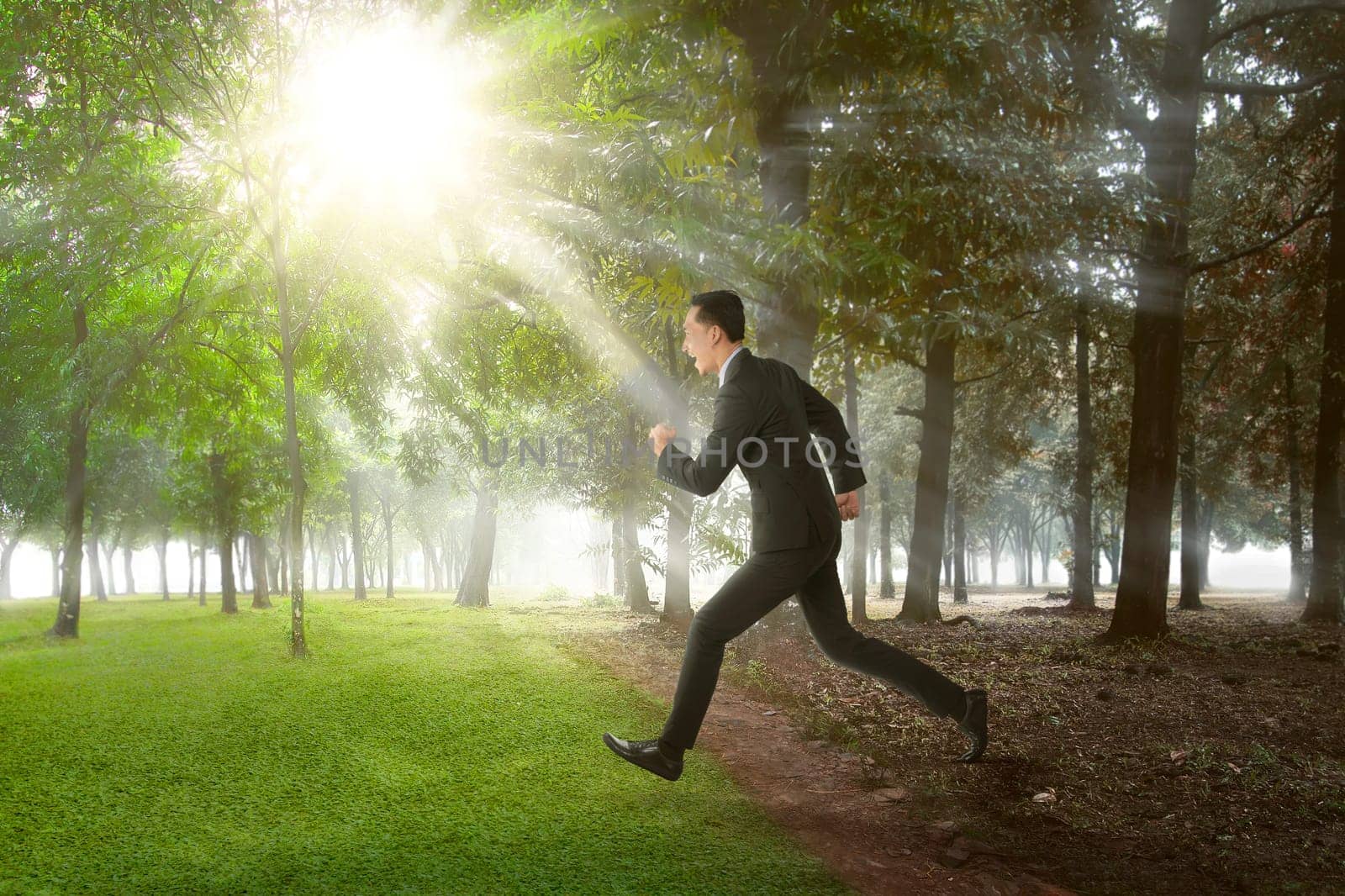 Happy asian businessman running on summer field on sunny day