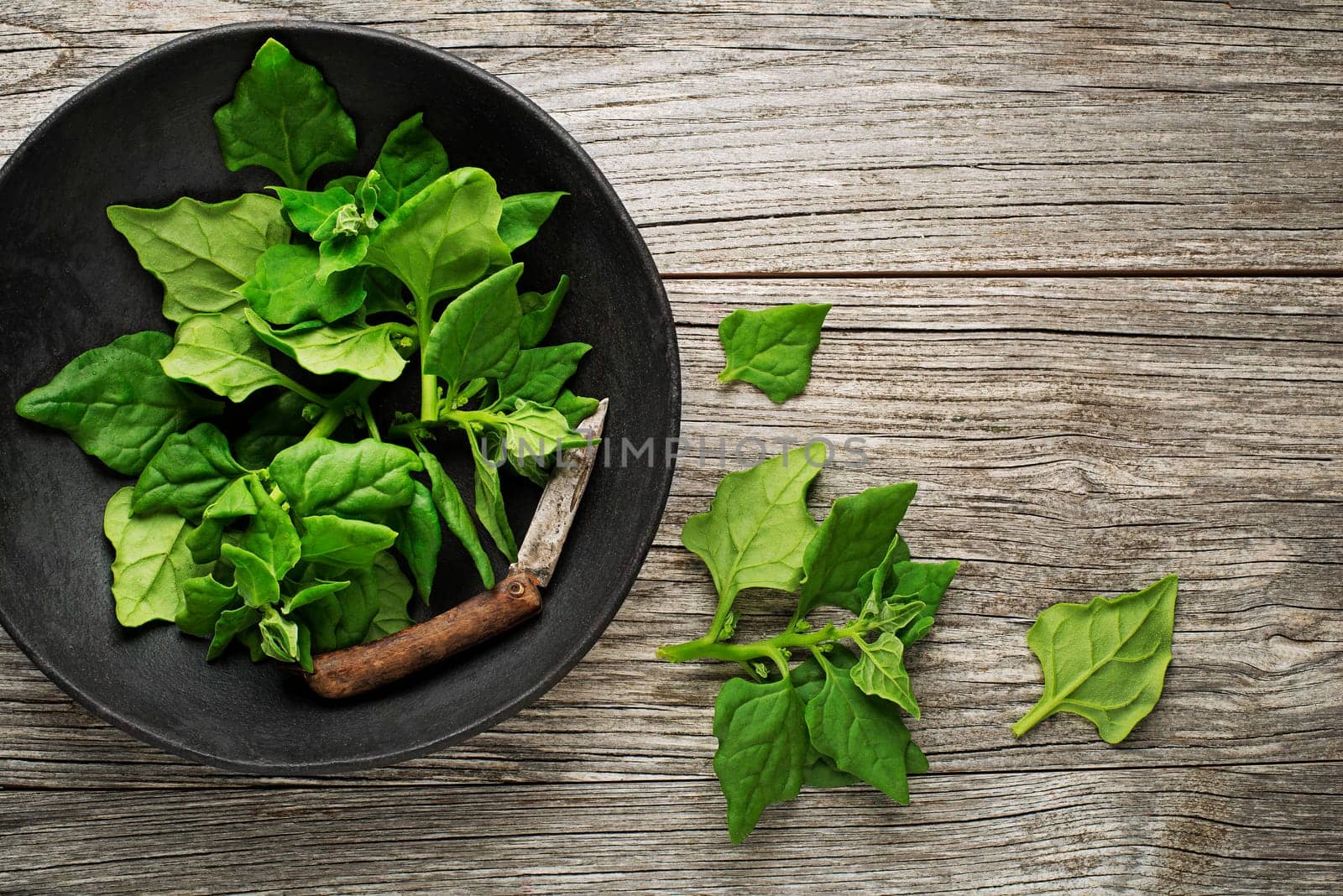 Fresh spinach leaves in bowl on rustic wooden table.