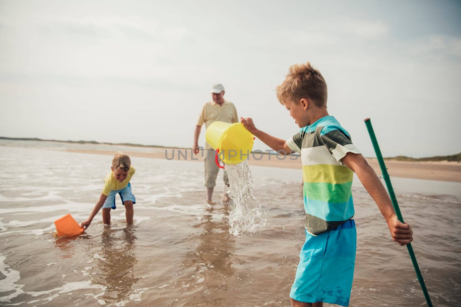 Rear view of little boys playing in the sea. Their grandad is standing close by watching over them.