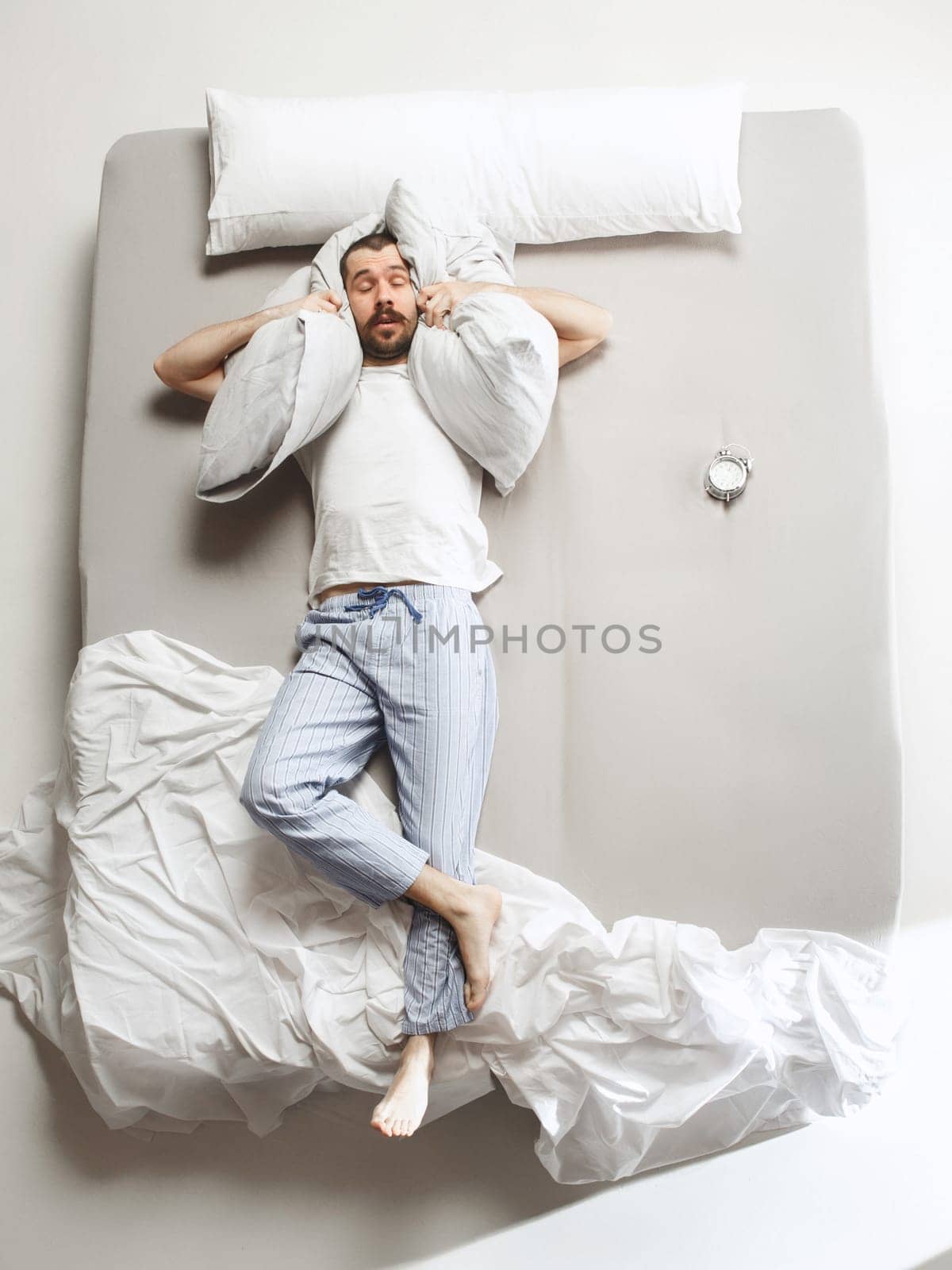 Top view photo of young man sleeping in a big white bed. Emotions concept. Morning after sleep. Happy man on the bed. alarm clock and unwillingness to wake up