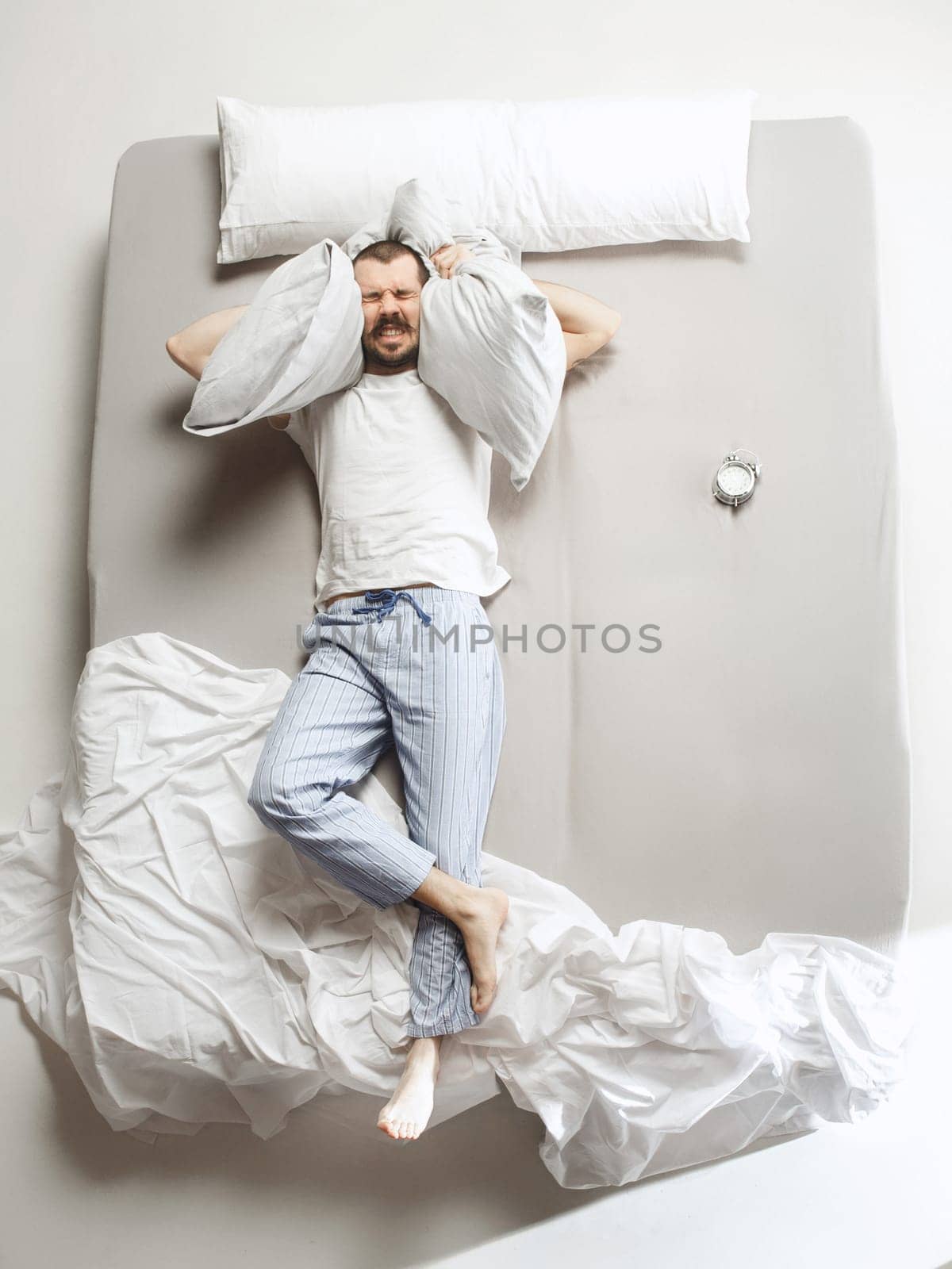 Top view photo of young man sleeping in a big white bed. Emotions concept. Morning after sleep. Happy man on the bed. alarm clock and unwillingness to wake up