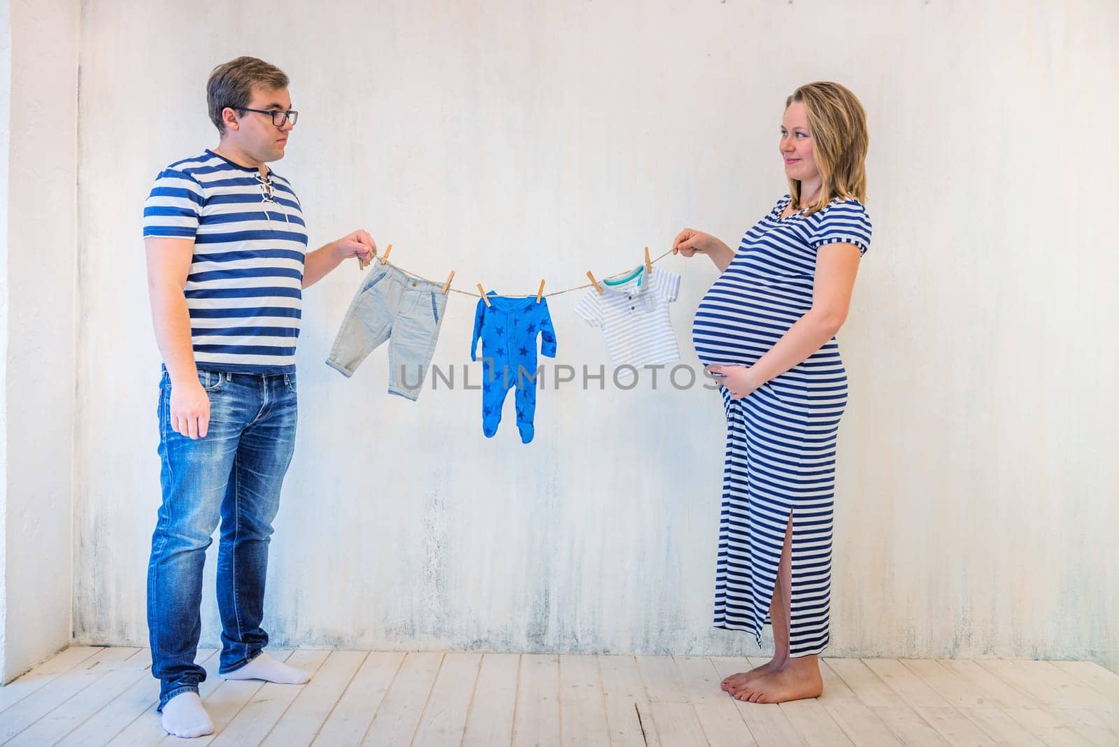 Young couple: pregnant woman and man holding baby clothes