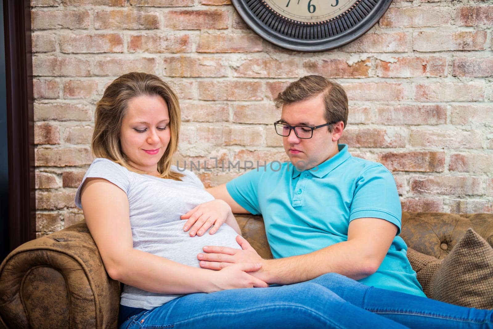 Happy pregnant woman and man sitting near brick wall