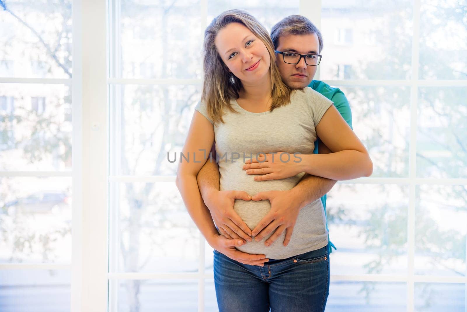 Beautiful couple: pregnant woman and man standing near window