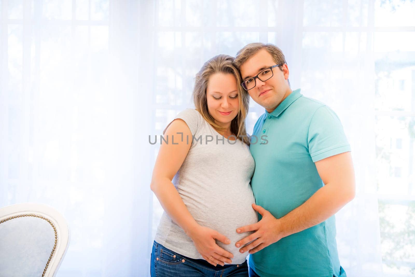 Beautiful couple: pregnant woman and man standing near window