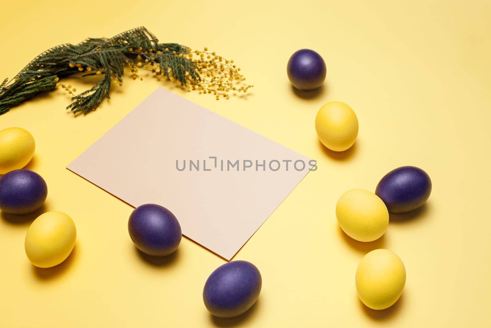 Beautiful easter table setting composition. A row of lilac and yellow color eggs on yellow background. Happy Easter greeting card. Top view, copy space.