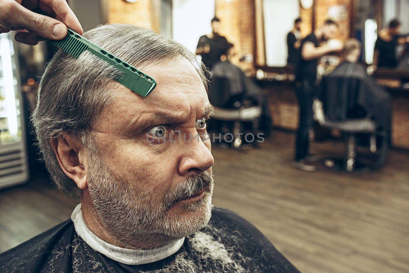 The hands of barber making haircut of attractive old bearded man in barbershop