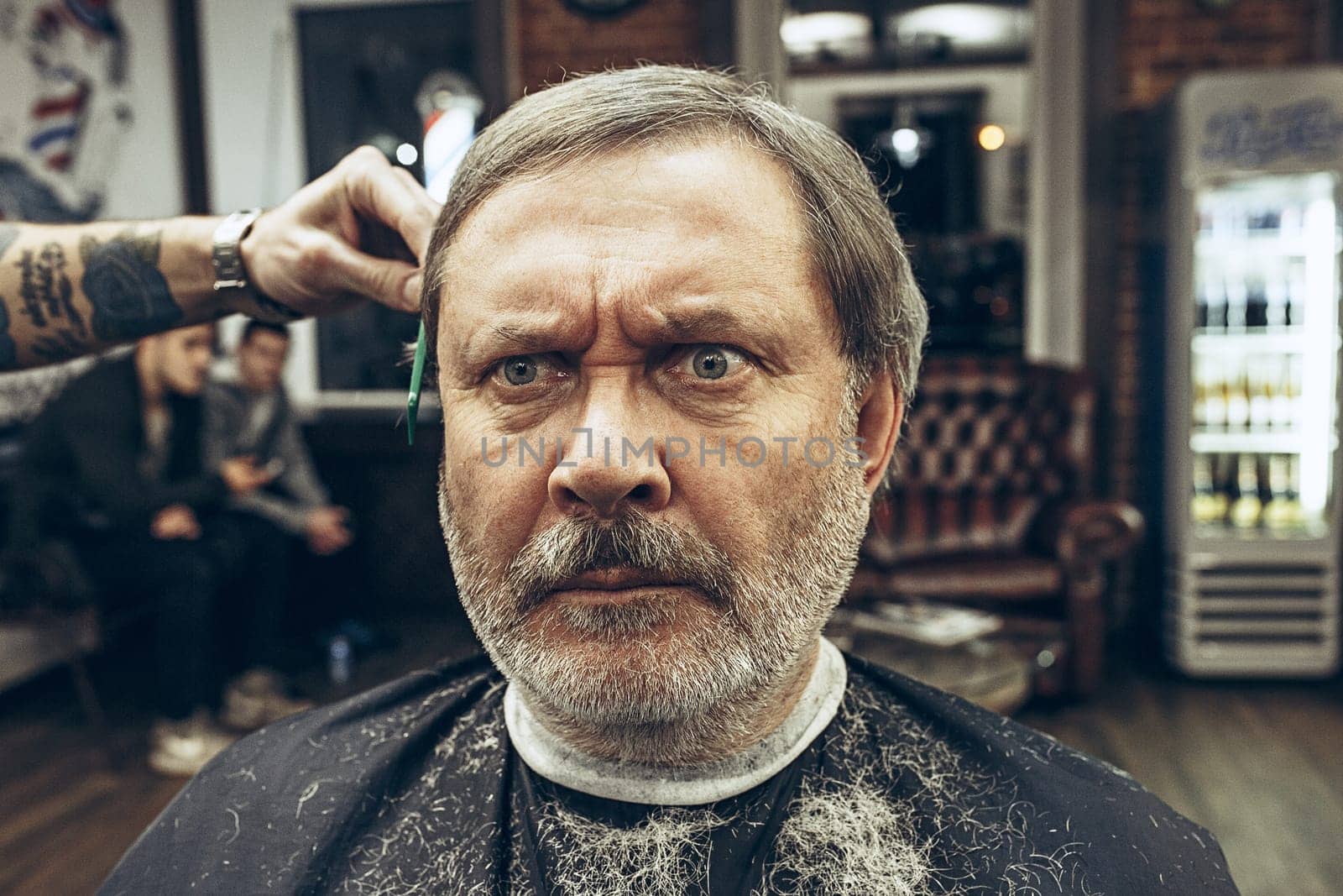 The hands of barber making haircut of attractive old bearded man in barbershop