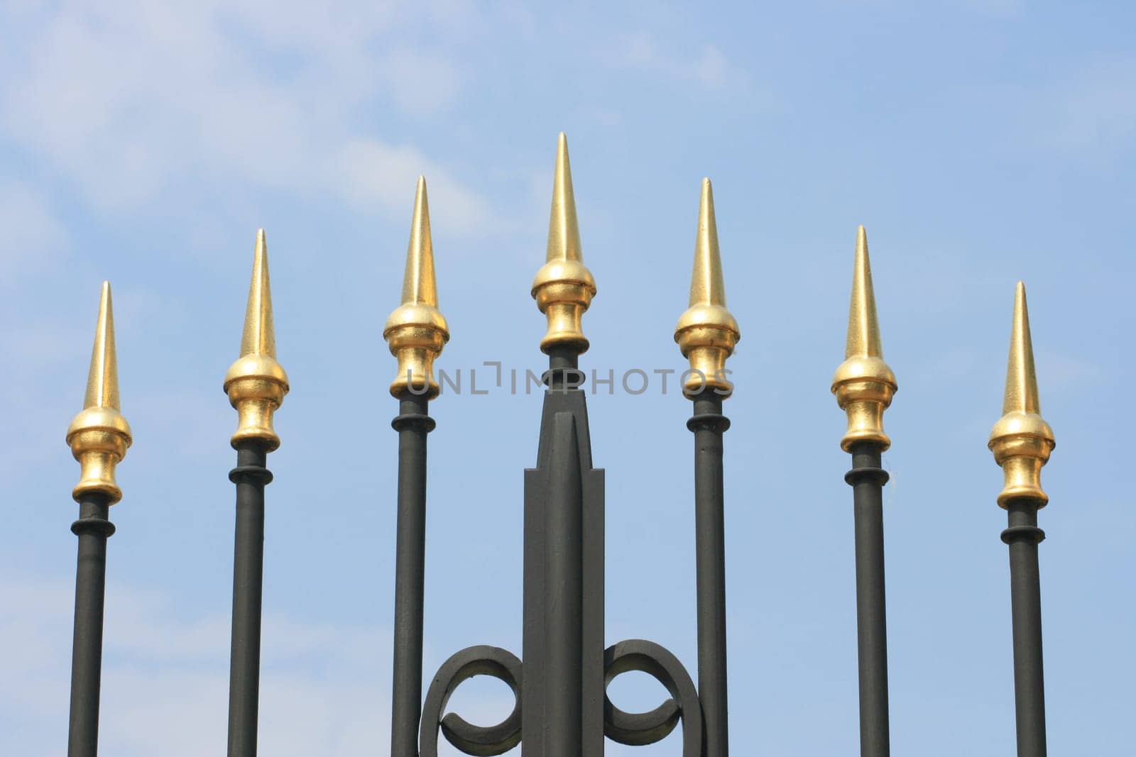 Wrought iron spikes of a gate, with a blue sky background