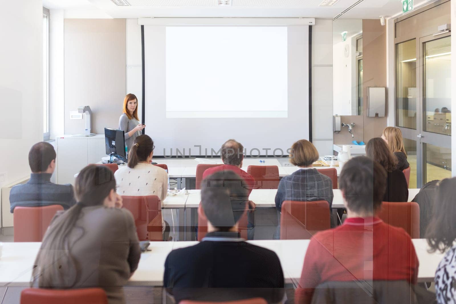 Speaker giving presentation in lecture hall at university. Participants listening to lecture and making notes. Copy space for brand on white screen.