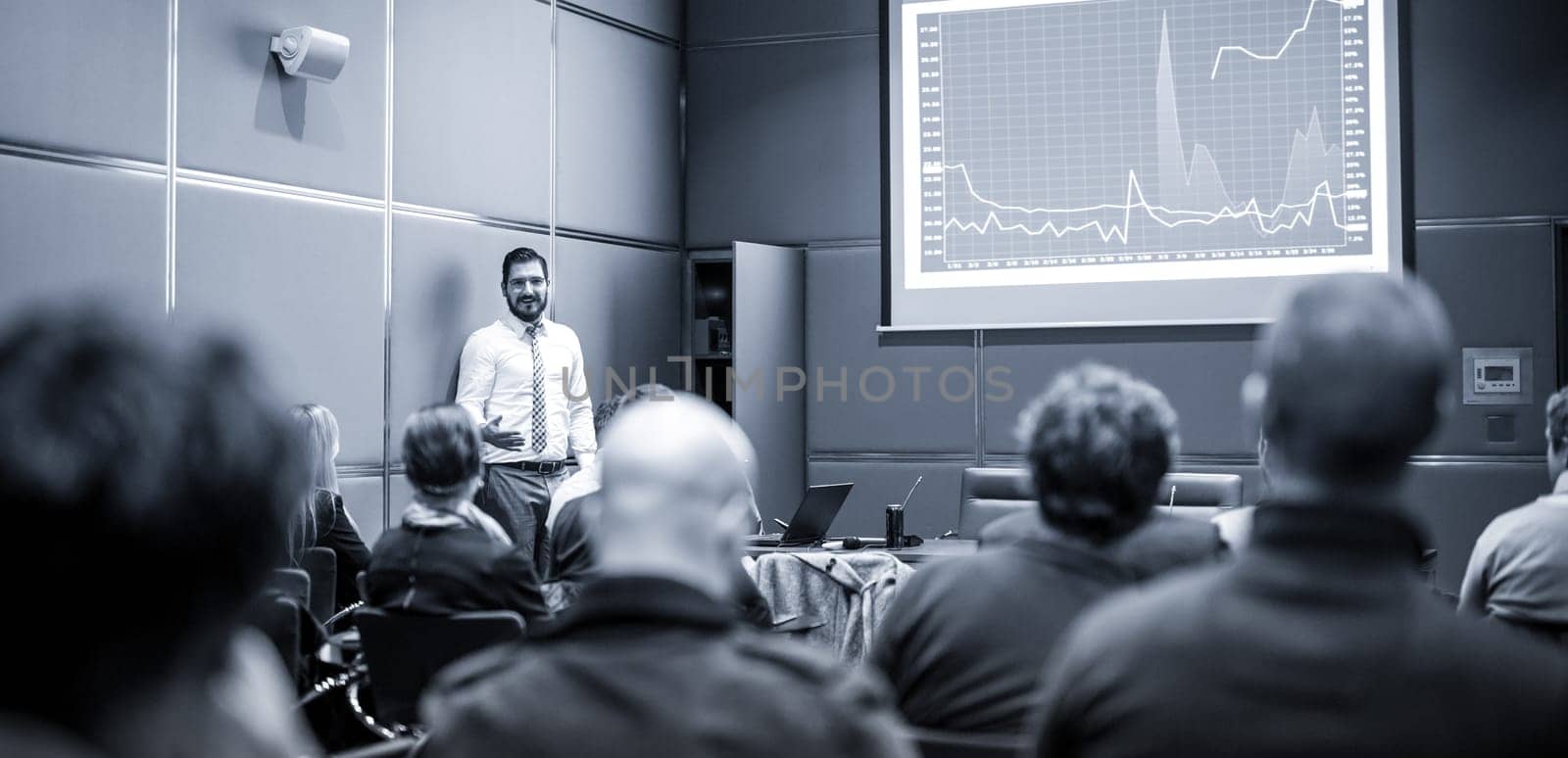 Public Speaker Giving a Talk at Business Meeting. Audience in the conference hall. Business and Entrepreneurship concept. Blue toned black and white image.