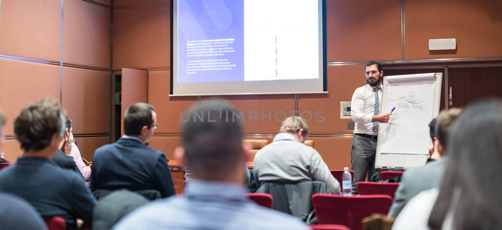 Public Speaker Giving a Talk at Business Meeting. Audience in the conference hall. Skilled coach asks questions to participants of business training. Business and Entrepreneurship concept.