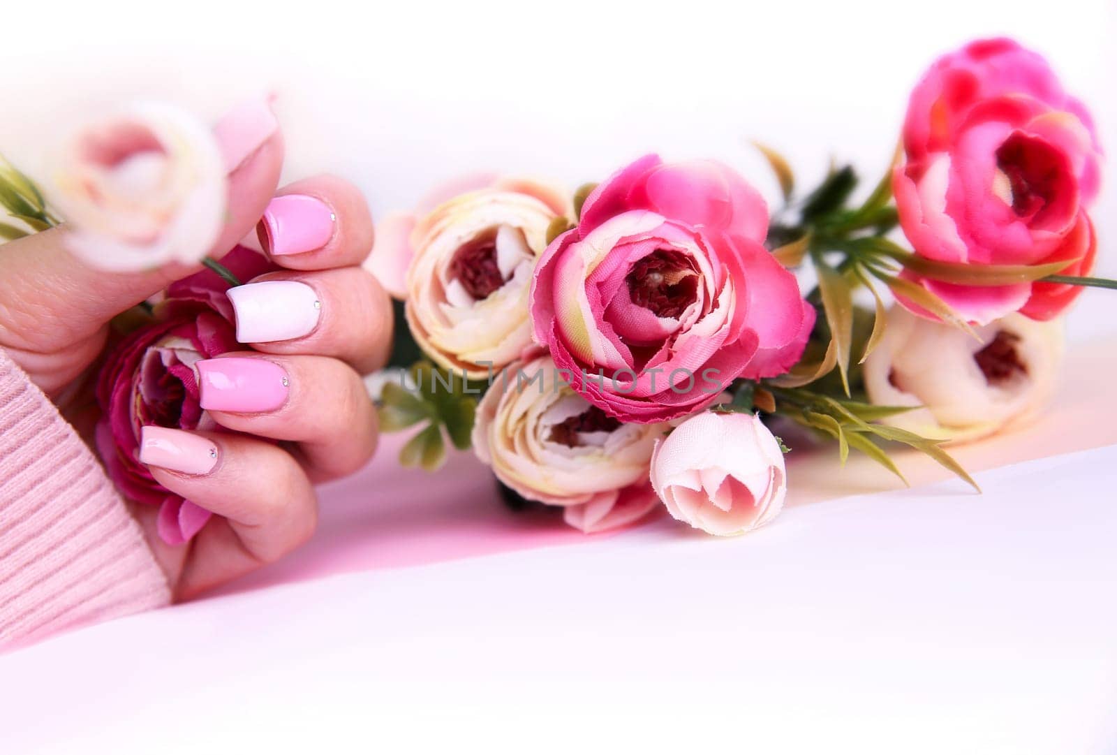 Nail design pink color. Manicured hand with flowers on table with empty copy space.