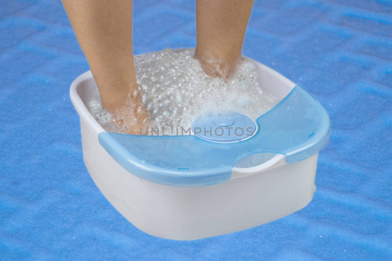 woman feet relax in foot bath in a vibrating foot massager on blue backround