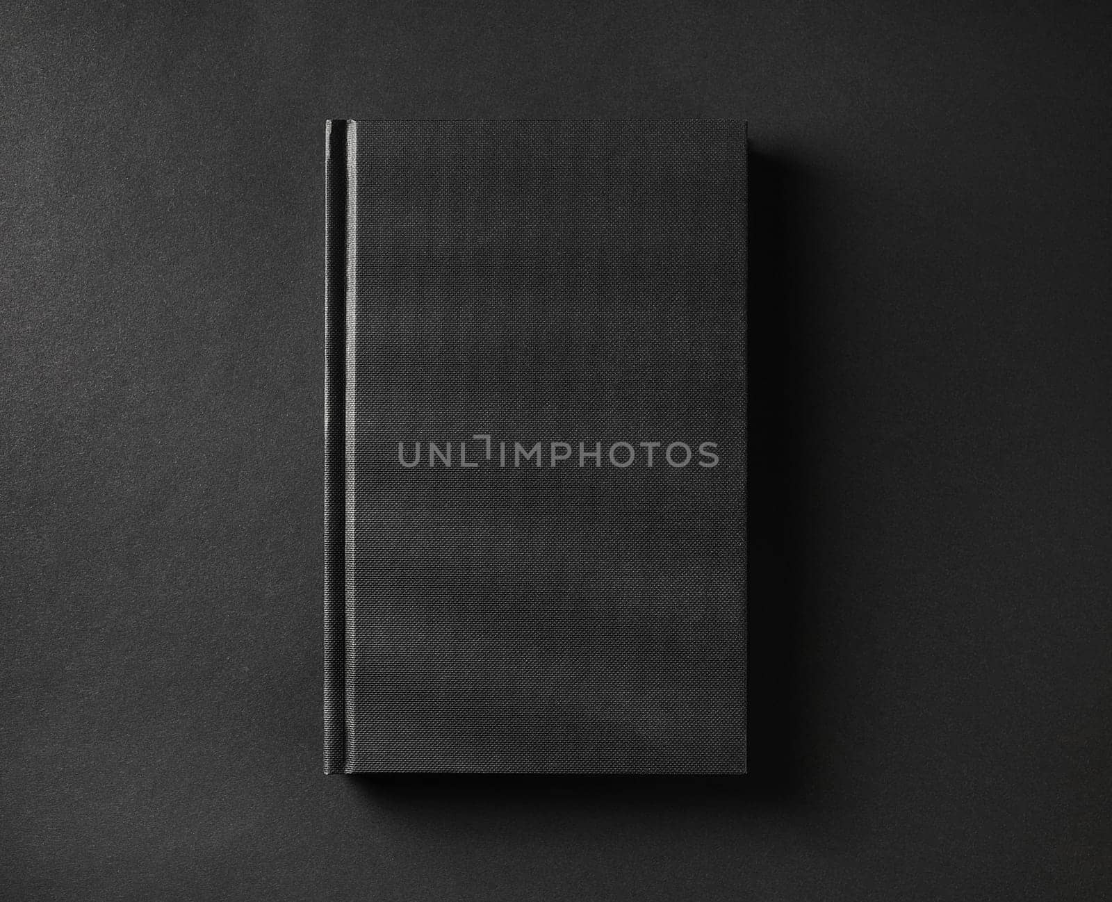 Photo of blank black book cover on black paper background. Flat lay.