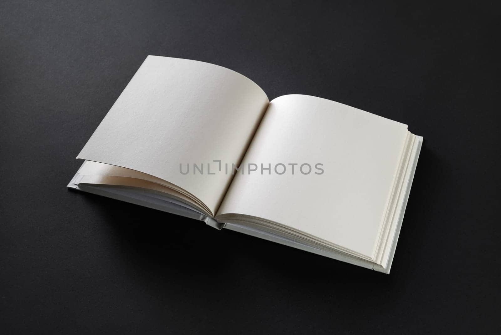 Open blank square book on black paper background.