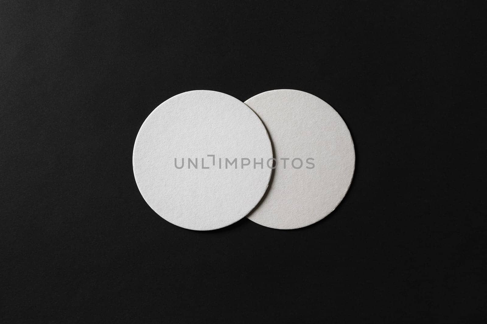 Two blank white beer coasters on black paper background. Responsive design mockup. Flat lay.