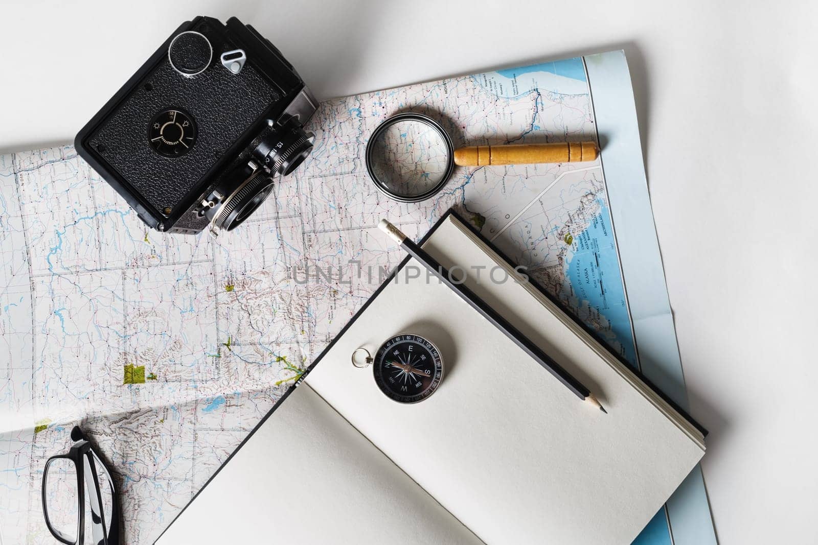 Making a travel plan. Map, blank notepad, camera, magnifier, compass, pencil and glasses. Flat lay.