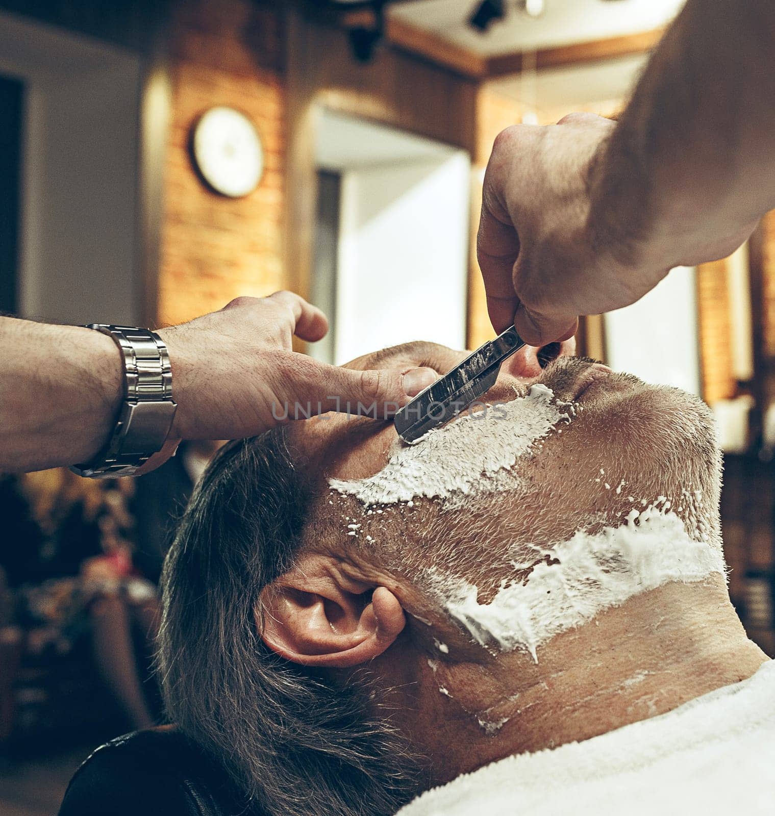 Close-up side top view handsome senior bearded caucasian man getting beard grooming in modern barbershop. Hairdresser serving client, making beard haircut using straight razor. Barber shop concept.