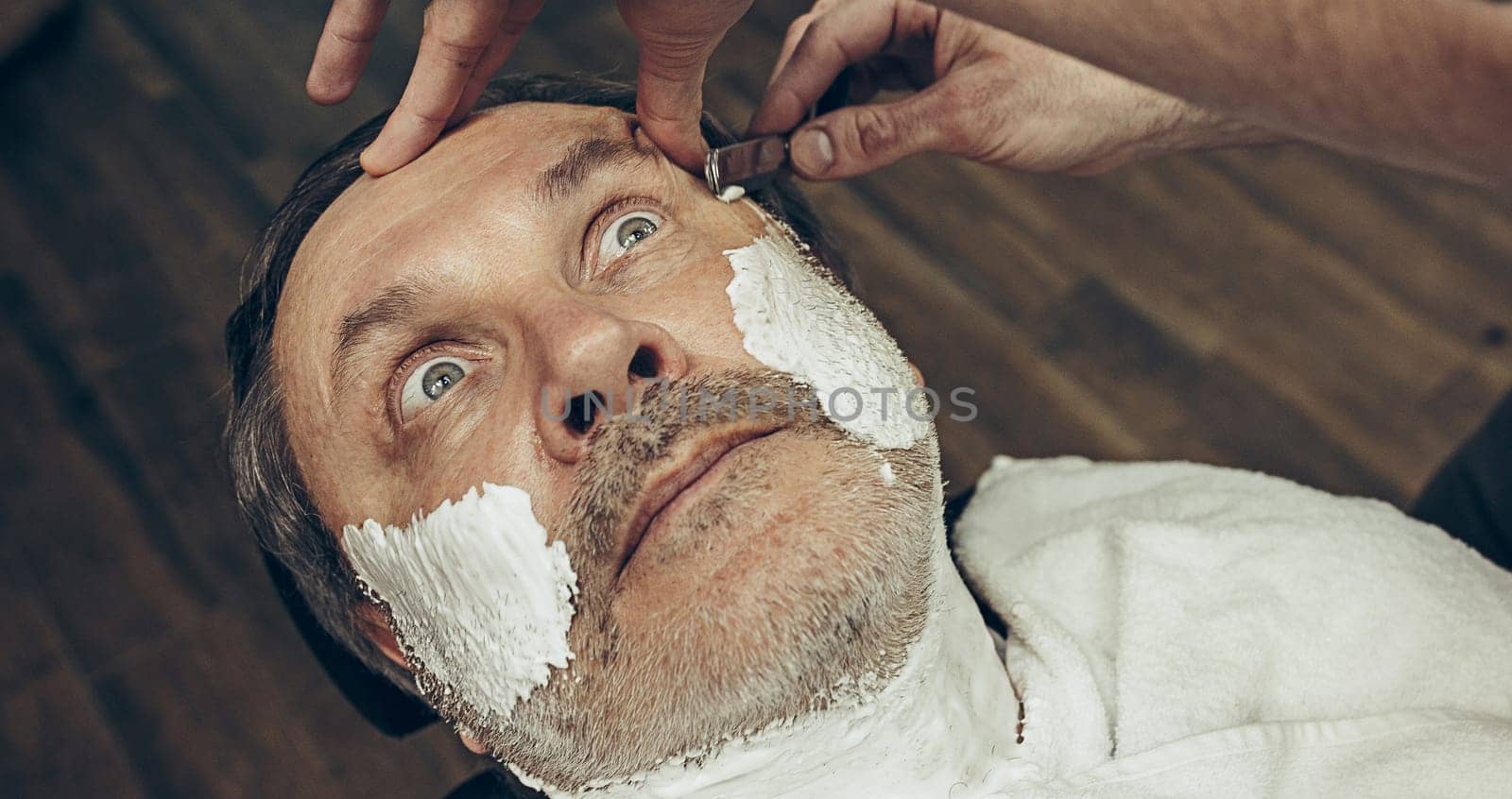 Close-up side top view handsome senior bearded caucasian man getting beard grooming in modern barbershop. Hairdresser serving client, making beard haircut using straight razor. Barber shop concept.