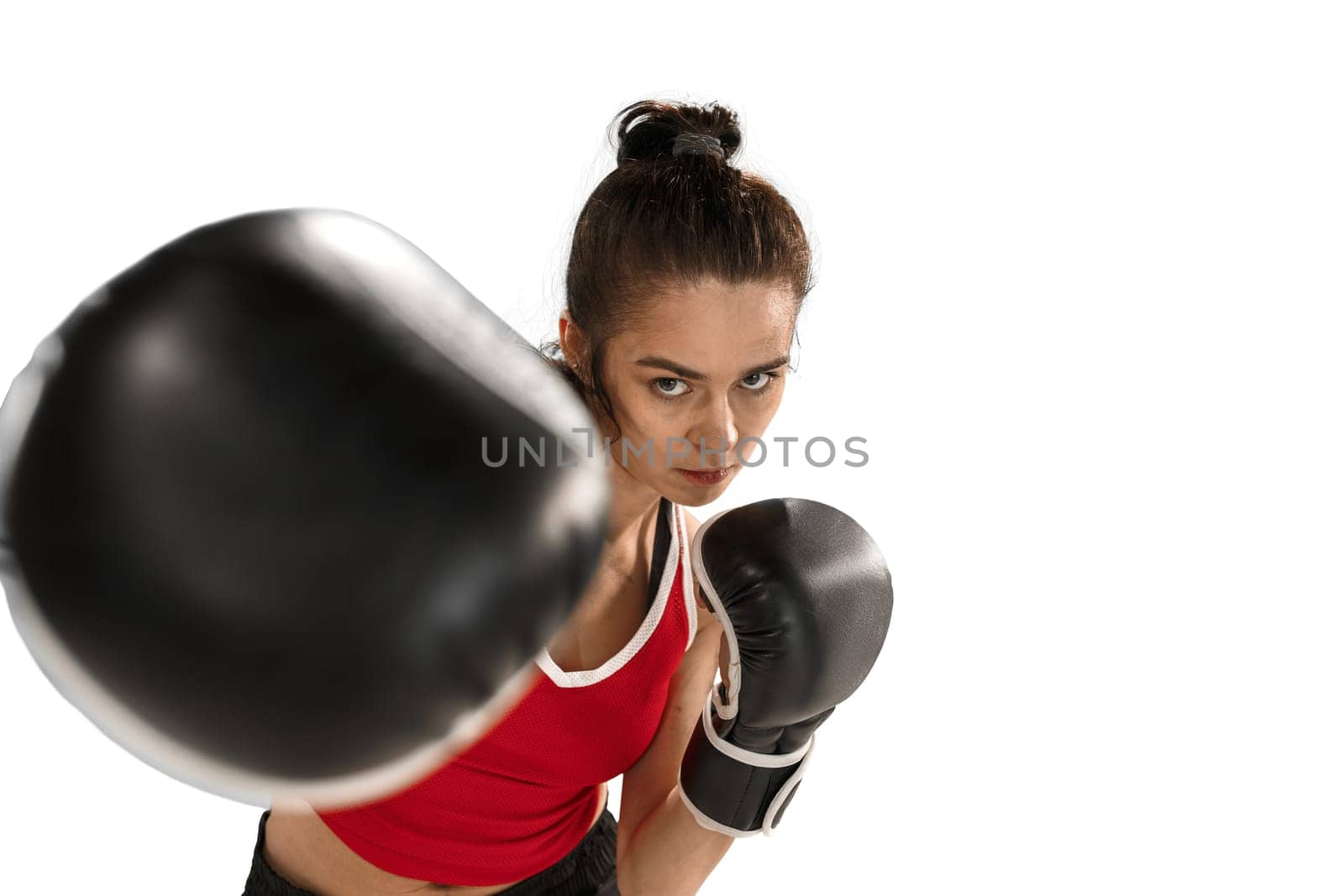 Young active beautiful woman with the black boxing gloves boxing at studio isolated on white background. Fitness, boxing concept. Female boxer. Human emotions. Caucasian model. head blow energy