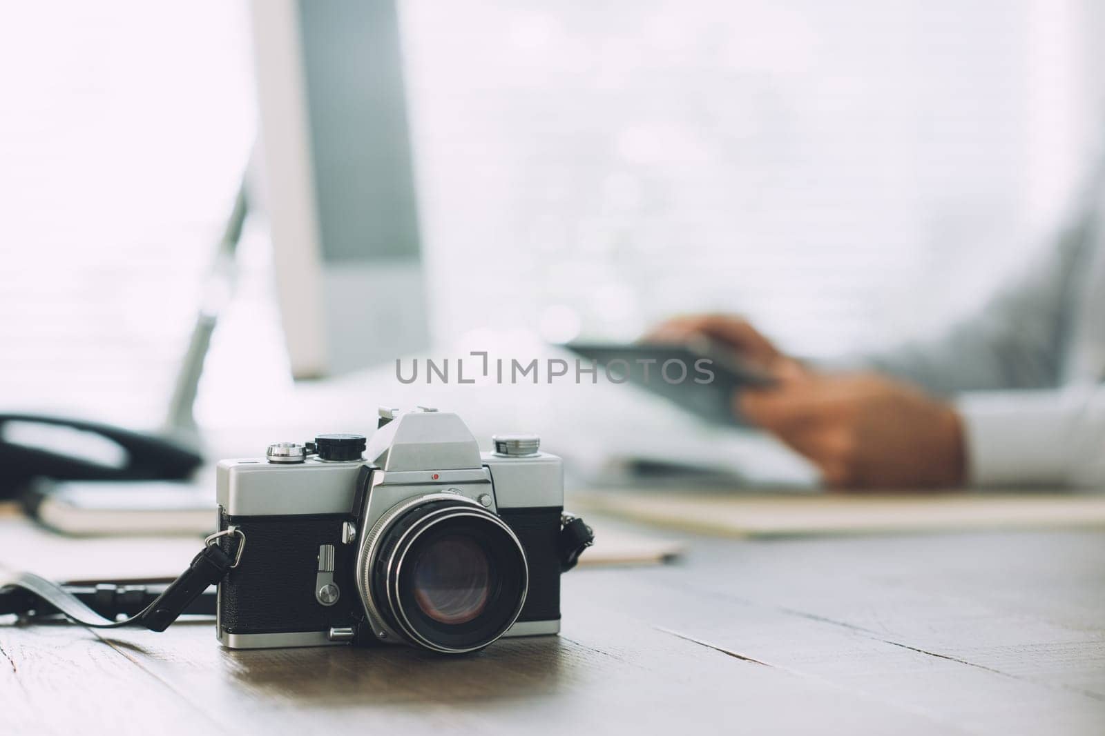 Professional photographer working with a computer at the communication agency and vintage camera on the foreground