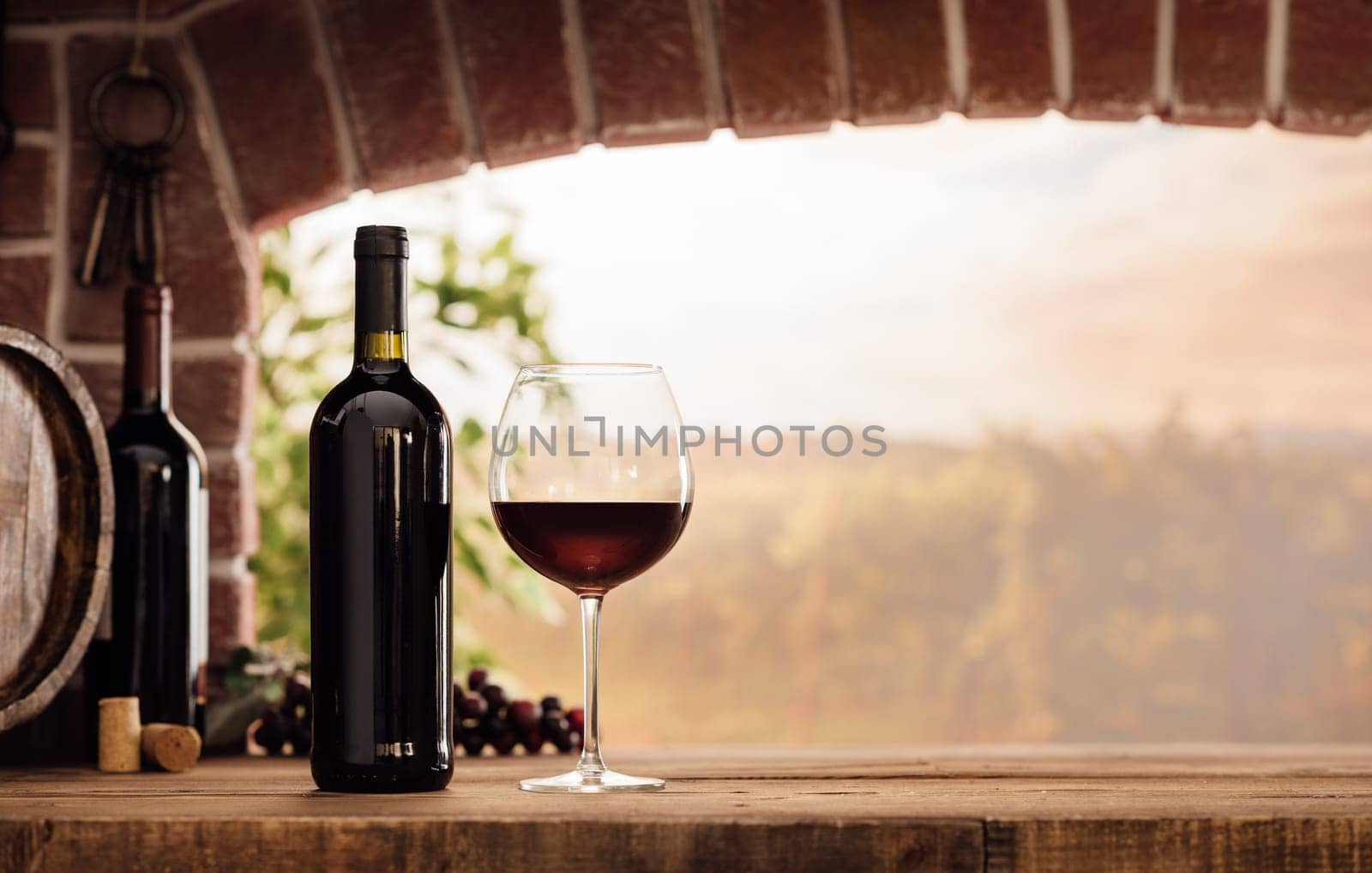Red wine tasting in the wine cellar: wineglass and bottles next to the window and panoramic view of vineyards at sunset