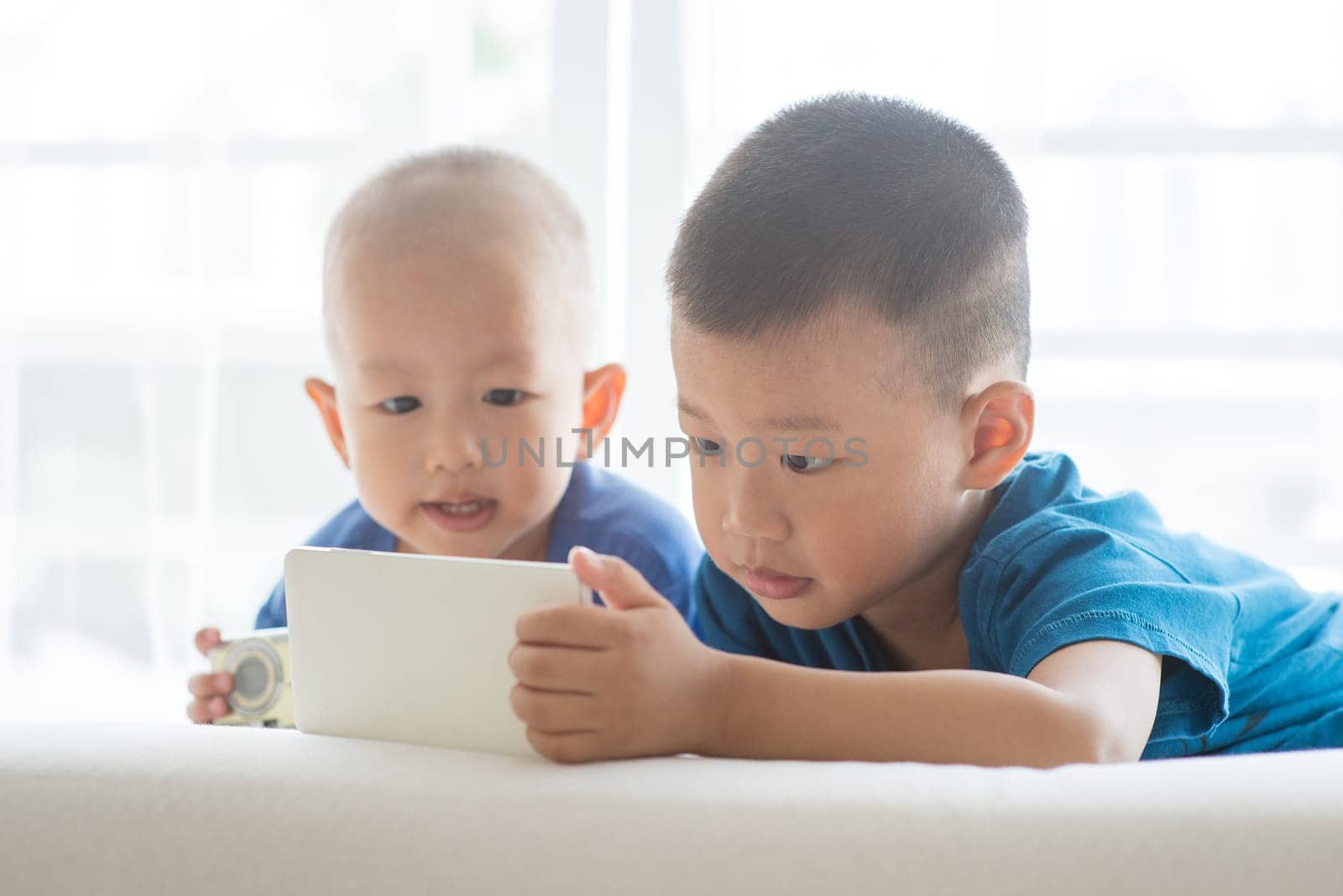 Young children addicted to technology gadget. Asian boys playing game with smart phone at home.