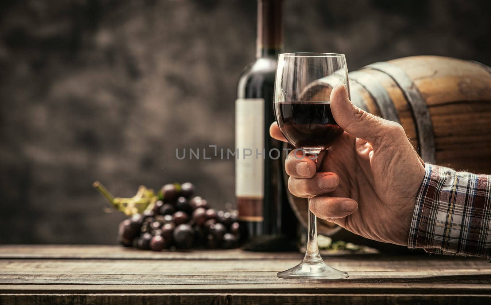 Senior wine maker tasting a glass of red wine in his cellar, wine bottle and wooden barrel on the background, wine tradition and culture concept