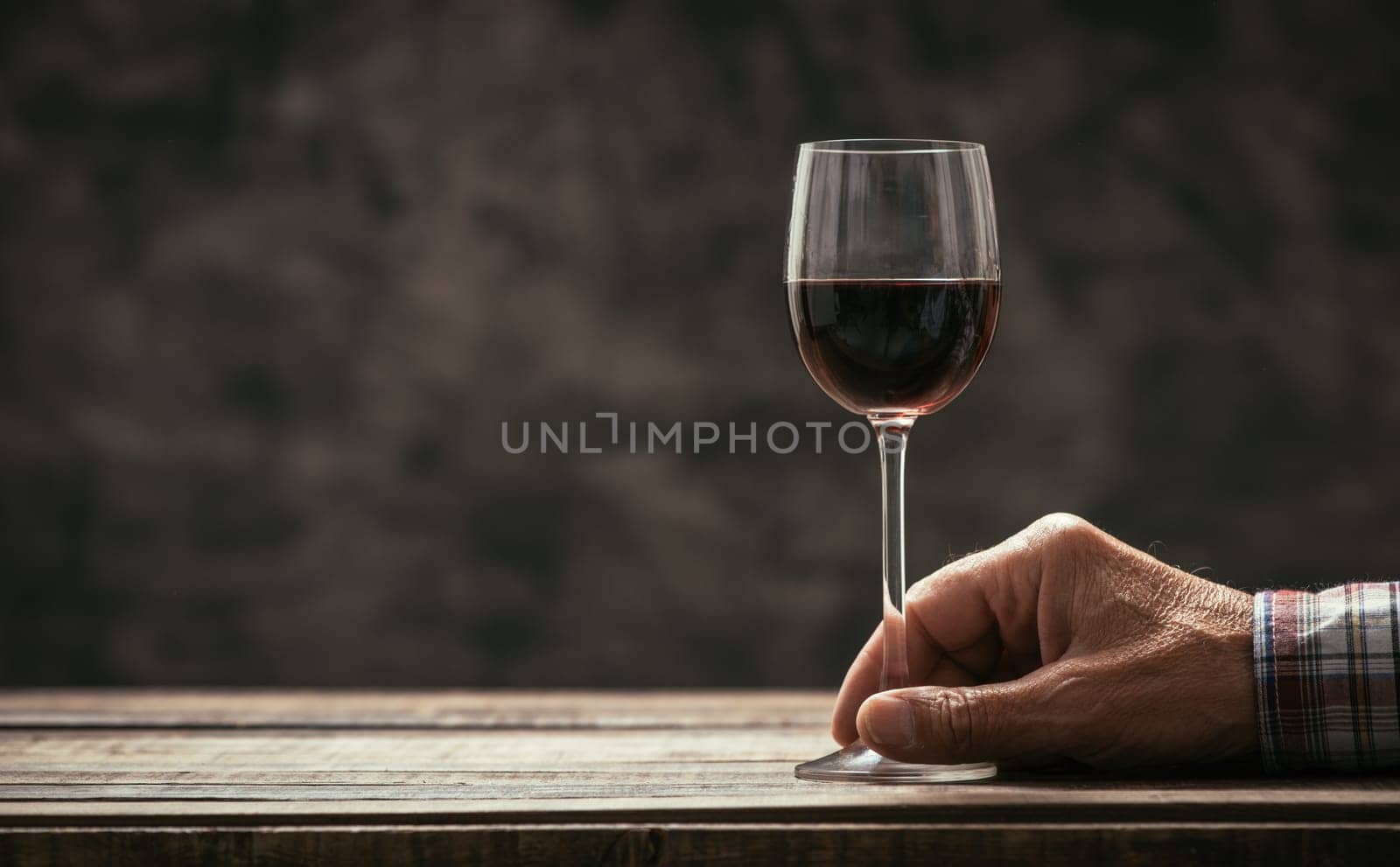 Senior man and wine expert tasting a glass of red wine in the cellar, hand close up, wine tradition and culture concept