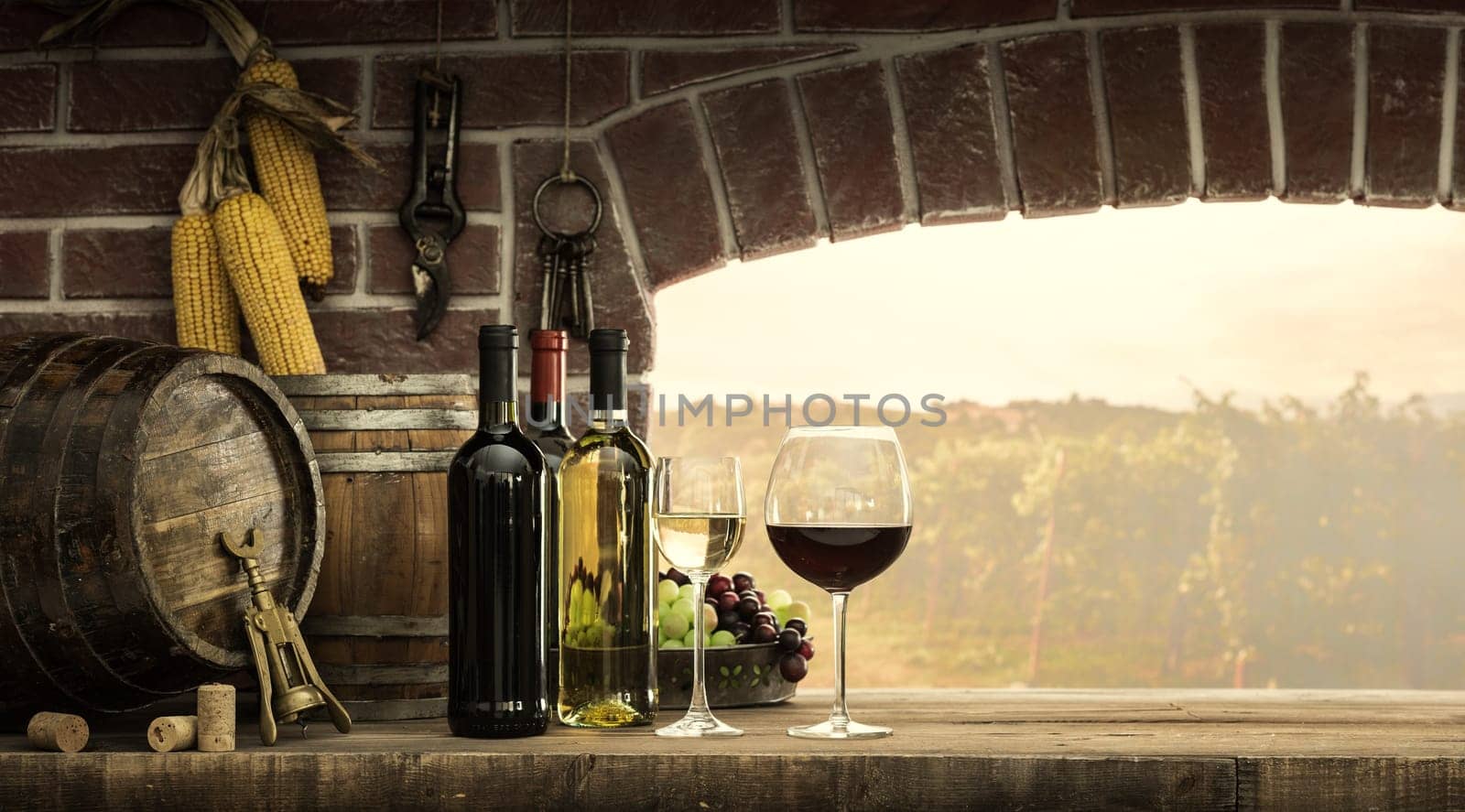 Wine bottles, wineglasses, barrels next to the cellar window and beautiful panoramic view of countryside vineyards: winemaking and wine culture concept