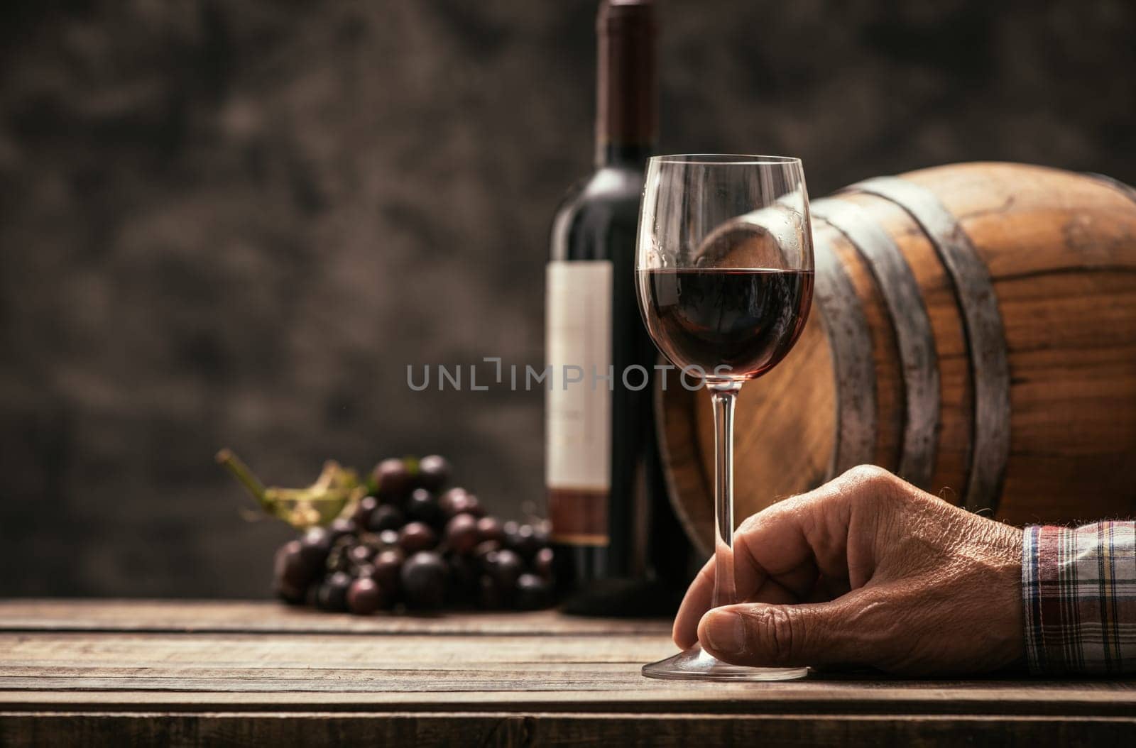 Senior wine maker tasting a glass of red wine in his cellar, wine bottle and wooden barrel on the background, wine tradition and culture concept