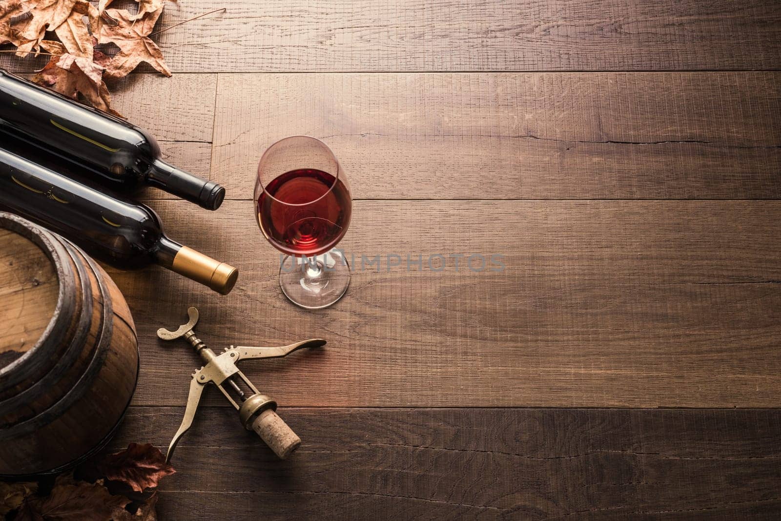 Excellent red wine bottles, wineglass, barrel and corkscrew on a rustic wooden table: traditional winemaking and wine tasting concept