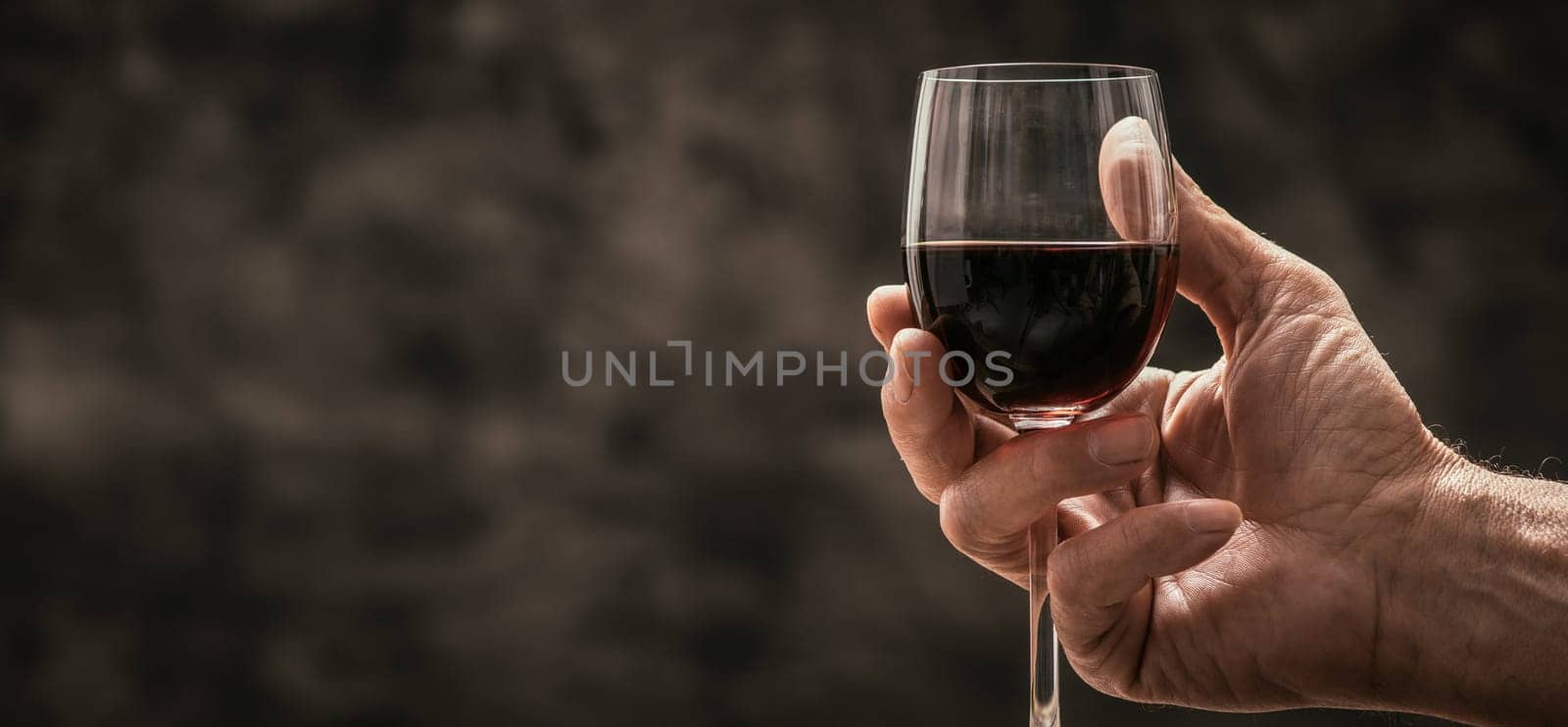 Senior wine expert tasting a glass of red wine in the cellar, hand close up, wine tradition and culture concept
