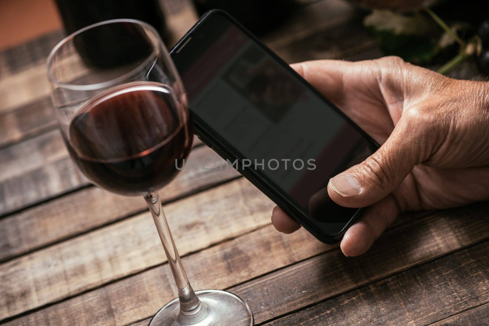 Man tasting a glass of red wine and using apps on his smartphone, wine culture and technology concept