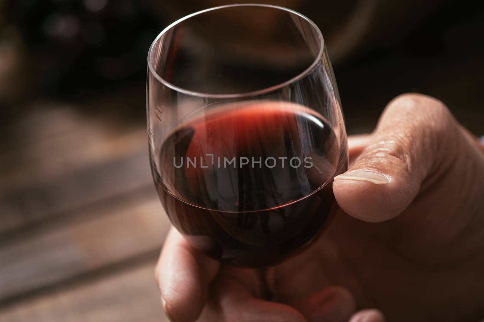Senior man tasting a glass of italian red wine, rustic wooden table on the background, hand close up