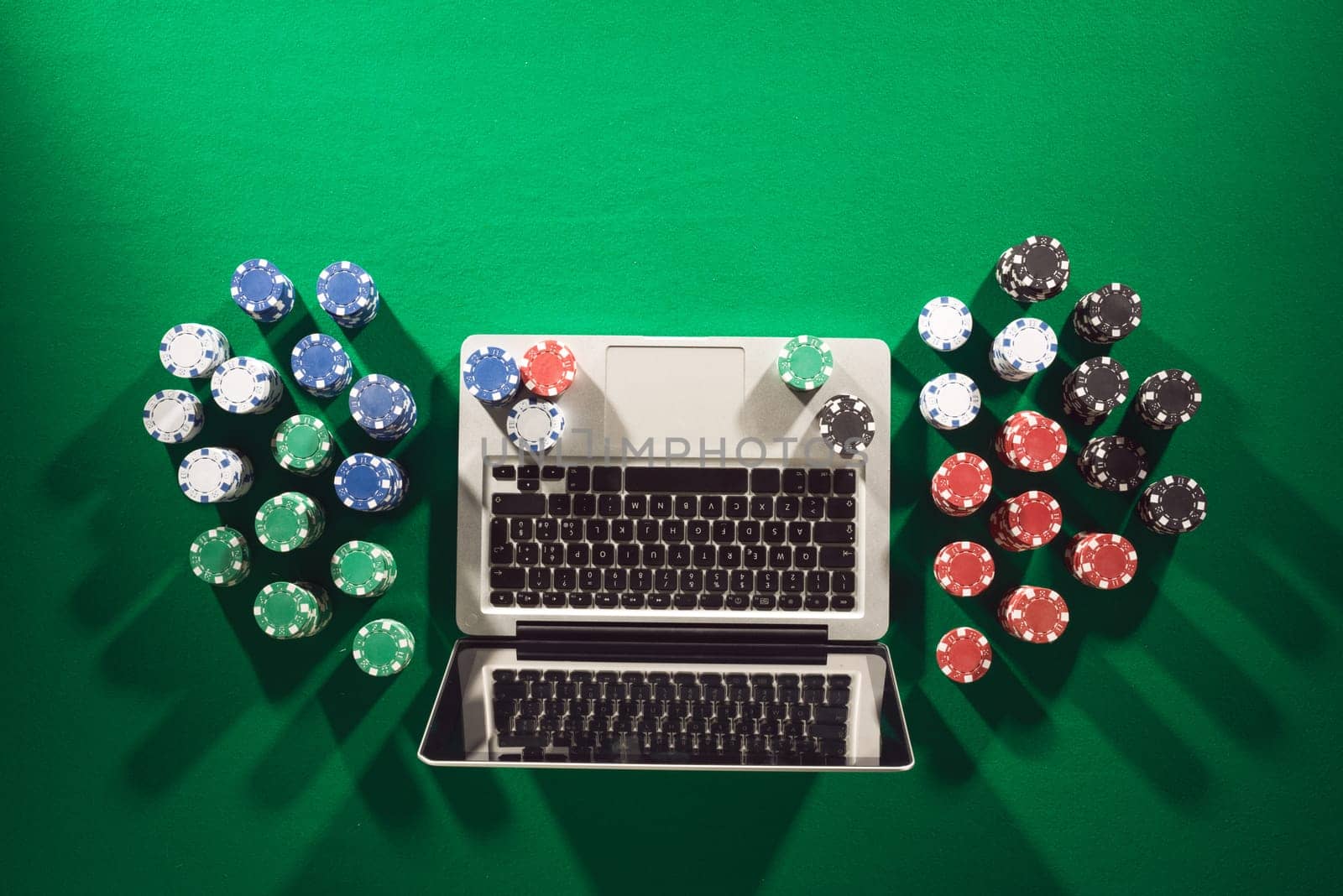 Poker and casino online gaming concept with laptop and stacks of chips on green table, top view