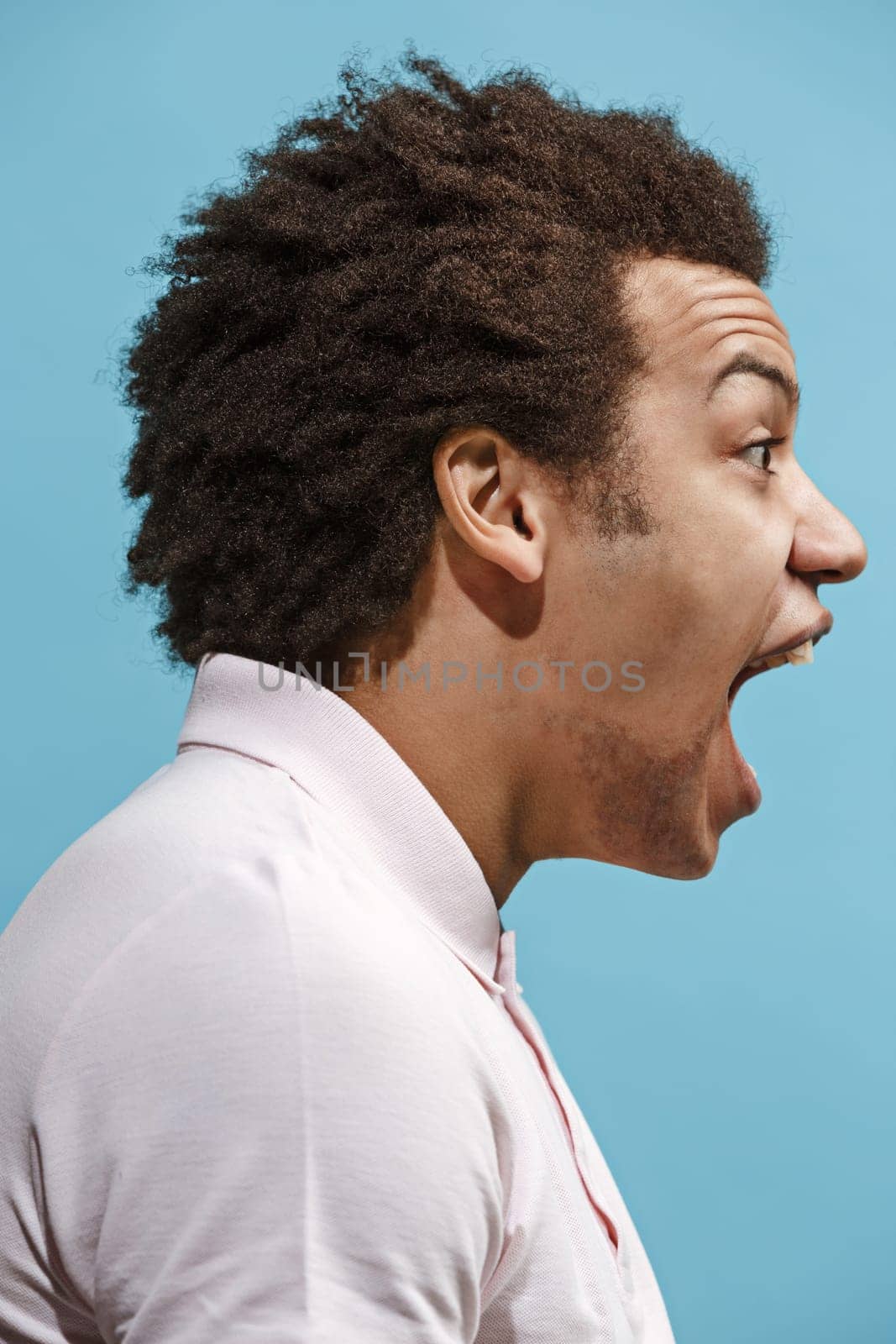 Screaming, hate, rage. Crying emotional angry man screaming on blue studio background. Emotional, young face. male half-length portrait. Human emotions, facial expression concept. Trendy colors. Profile