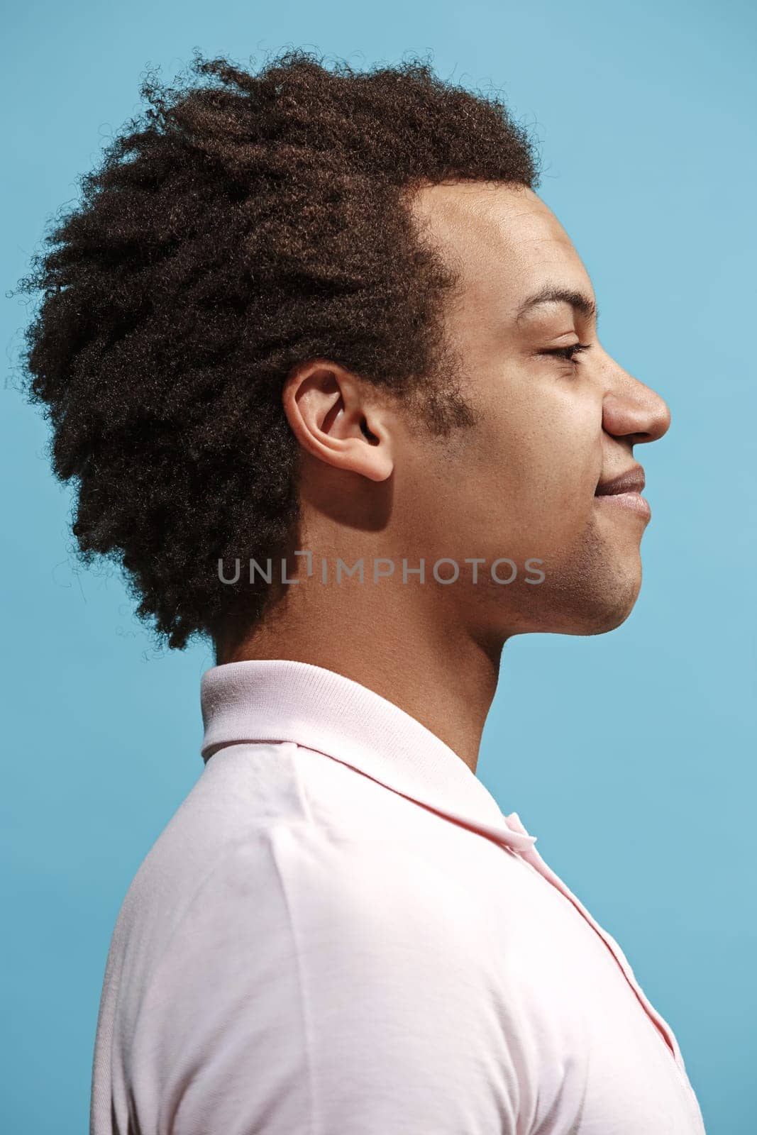 Happy business man standing and smiling isolated on blue studio background. Beautiful male half-length portrait. Young emotional man. The human emotions, facial expression concept. Profile view.