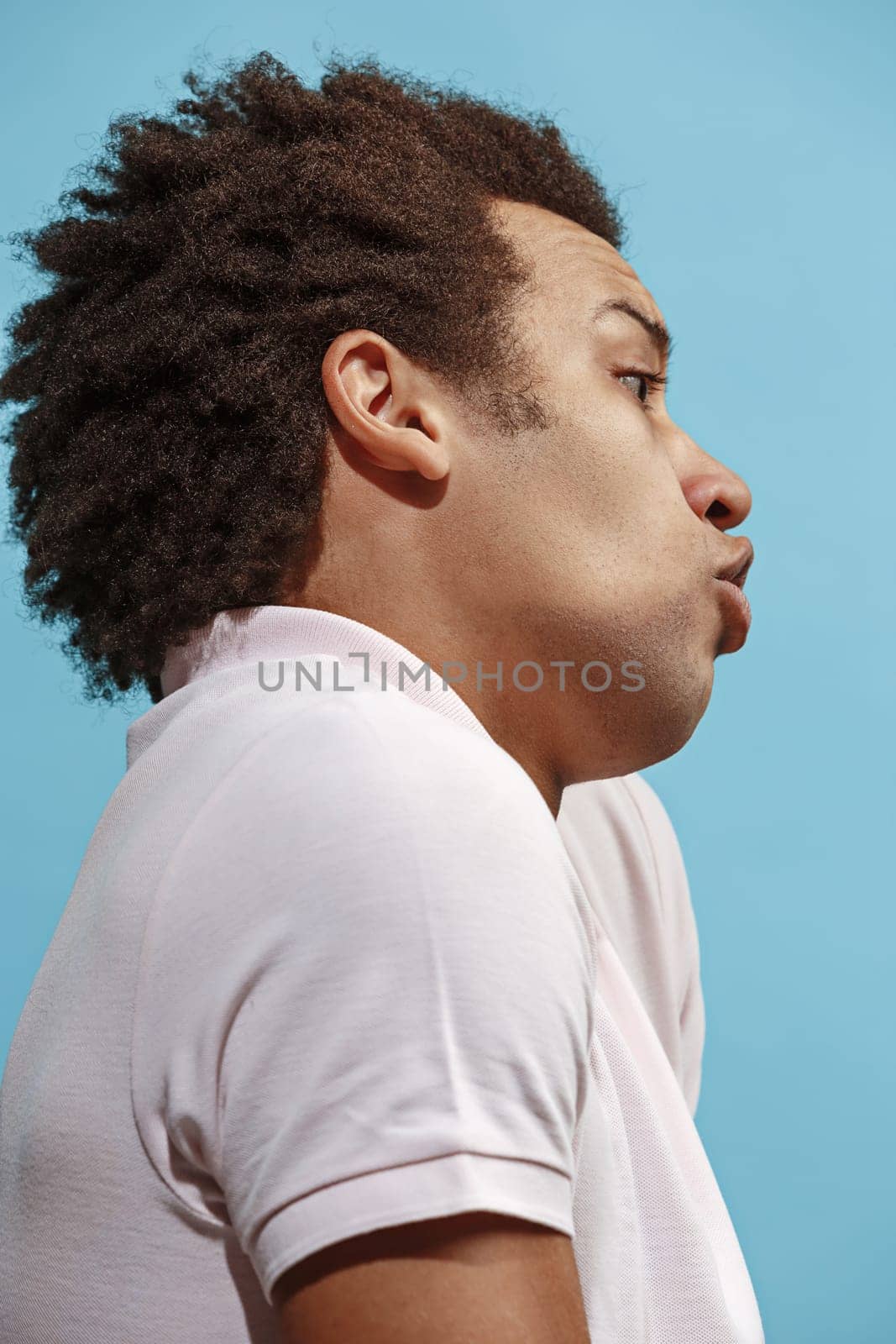 Argue, arguing concept. Beautiful male half-length portrait isolated on blue studio backgroud. Young emotional surprised afro man Human emotions, facial expression concept. Profile view