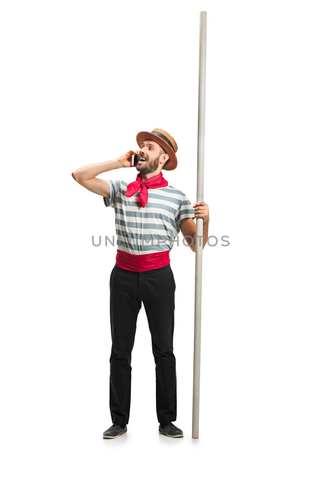 Caucasian funny bearded man in traditional gondolier costume and hat with paddle standing with mobile phone at studio isolated on white background. young man. Human emotions, facial expression concept