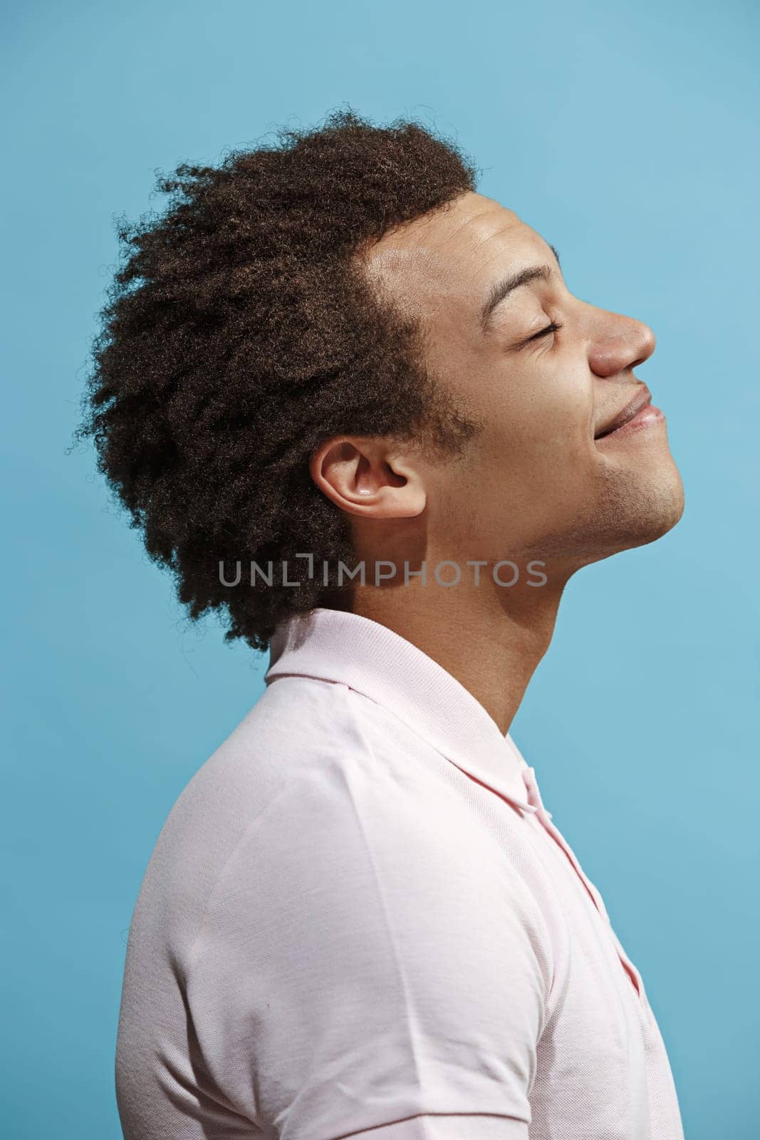 Happy business man standing and smiling isolated on blue studio background. Beautiful male half-length portrait. Young emotional man. The human emotions, facial expression concept. Profile view.