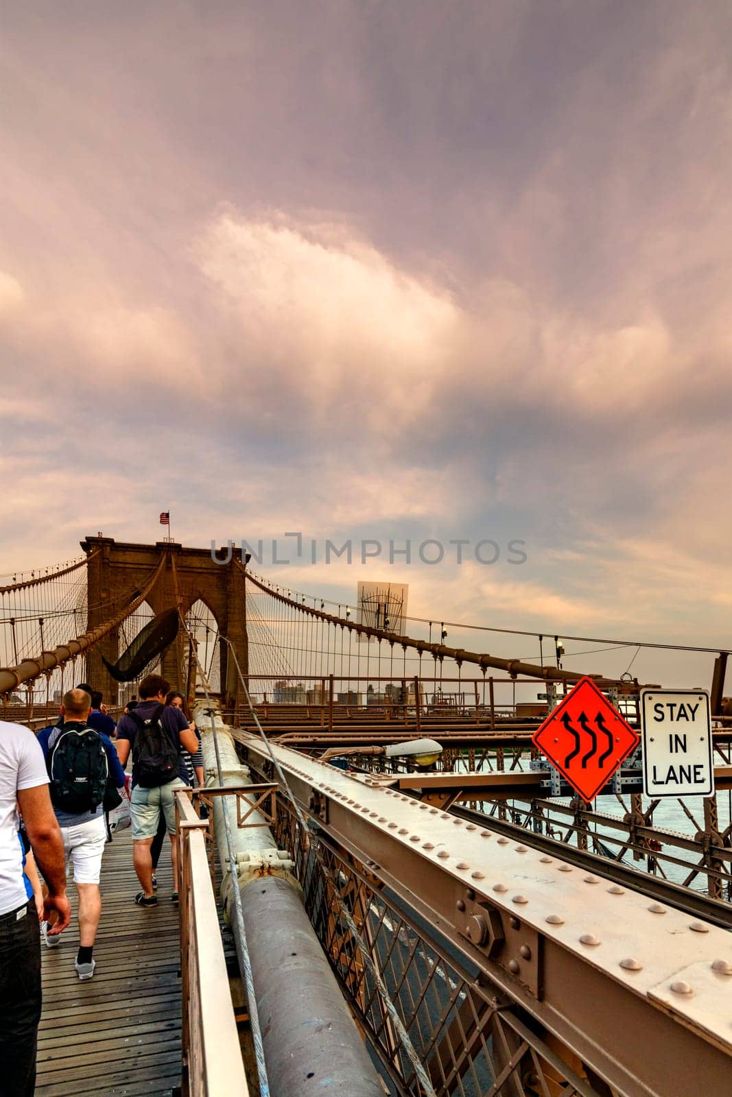 Brooklyn Bridge, New York, United States - June 08, 2015: People walk and while other tourists observe, from the bridge, the Manhattan skyline.