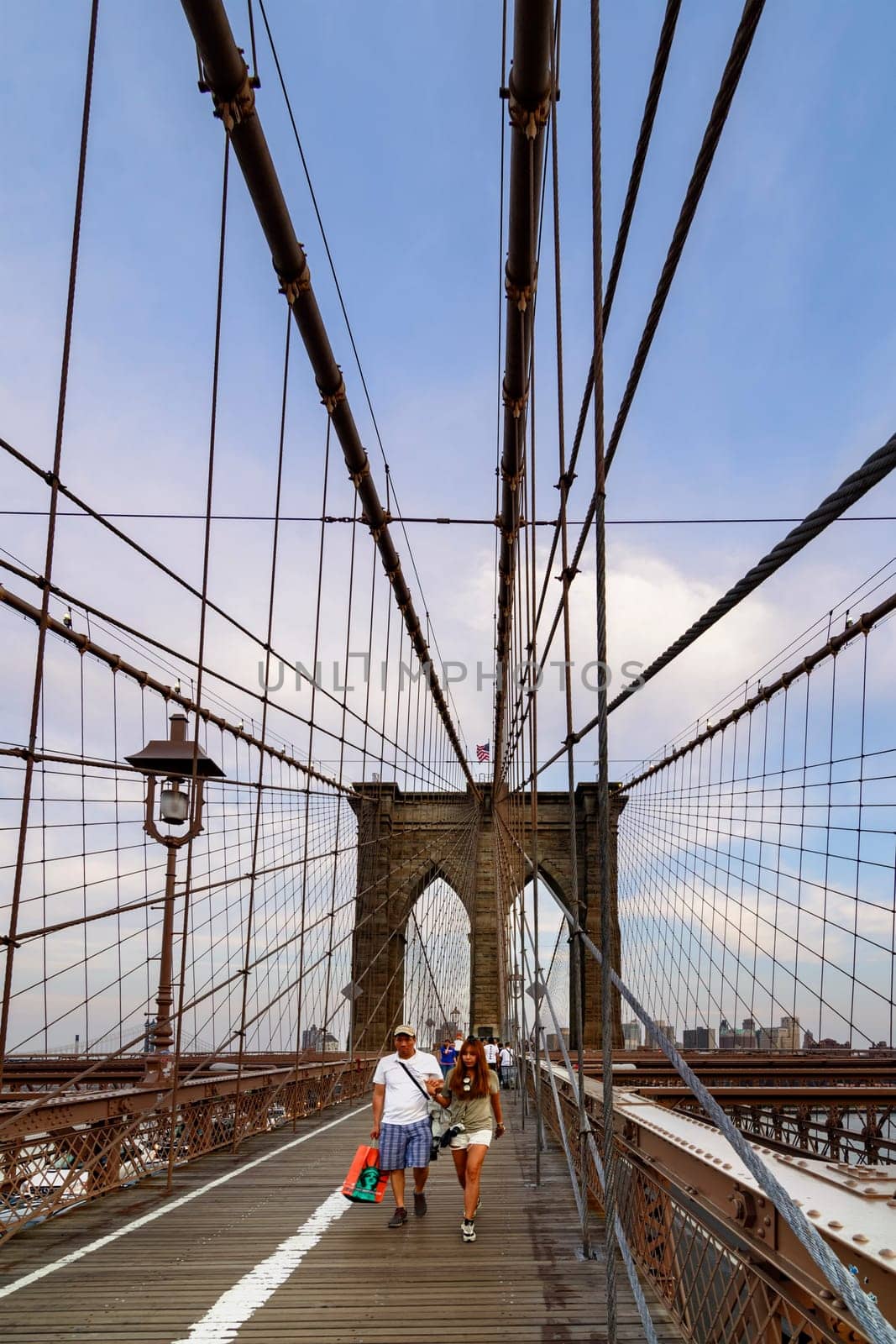 Brooklyn Bridge, New York, United States - June 08, 2015: People walk and while other tourists observe, from the bridge, the Manhattan skyline.