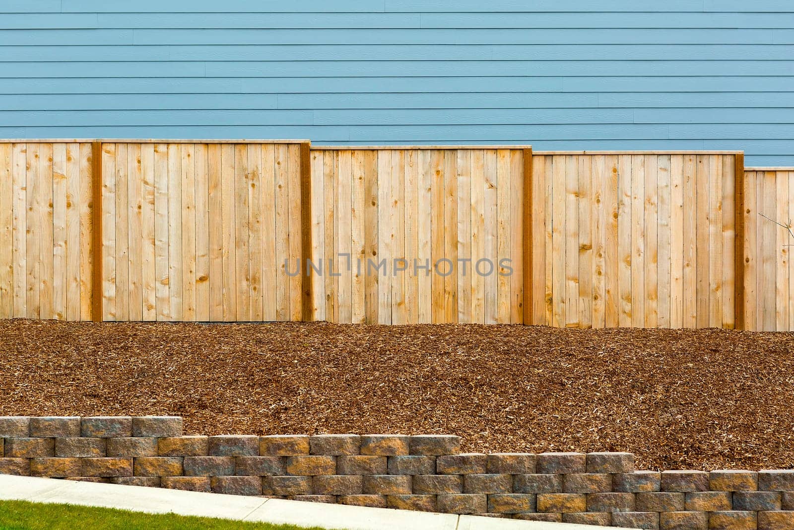 New Garden Wood Fence with house siding barkdust mulch concrete retaining wall along exterior sidewalk