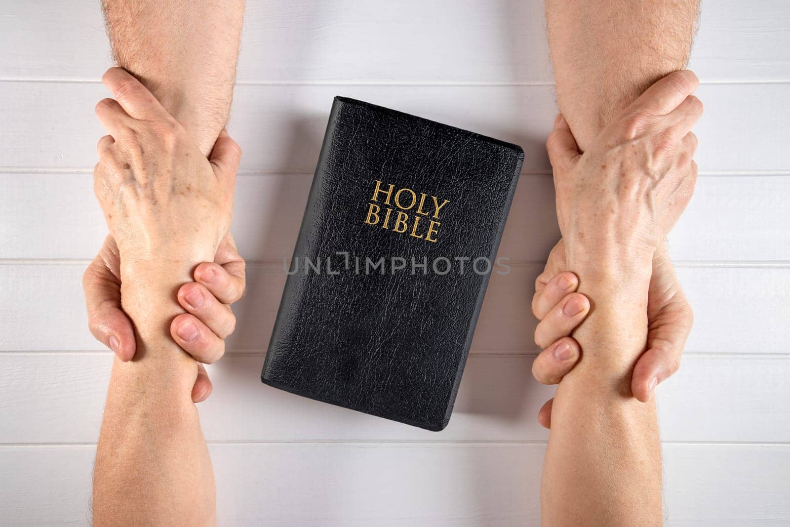 Old man and woman holding hands around a Holy Bible on white wood board