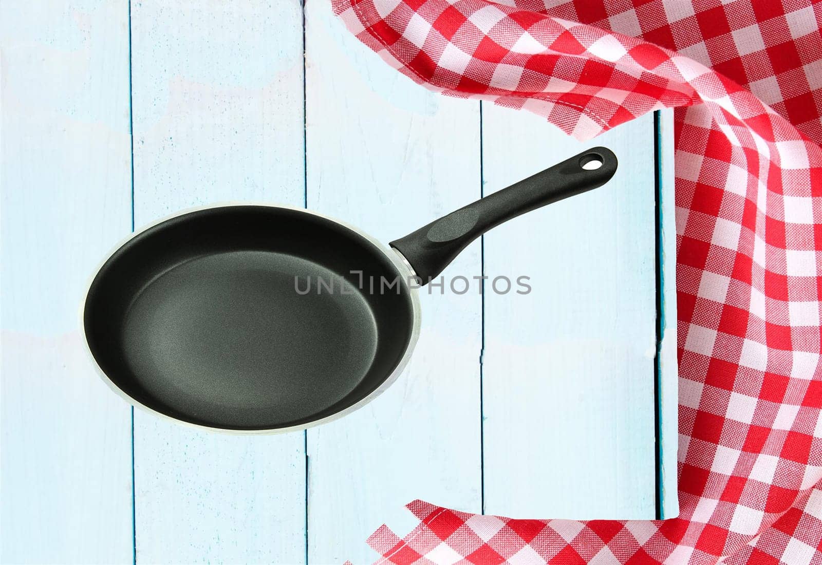 Empty pan and a red white checkered tablecloth on a wooden bright tabletop. concept food.